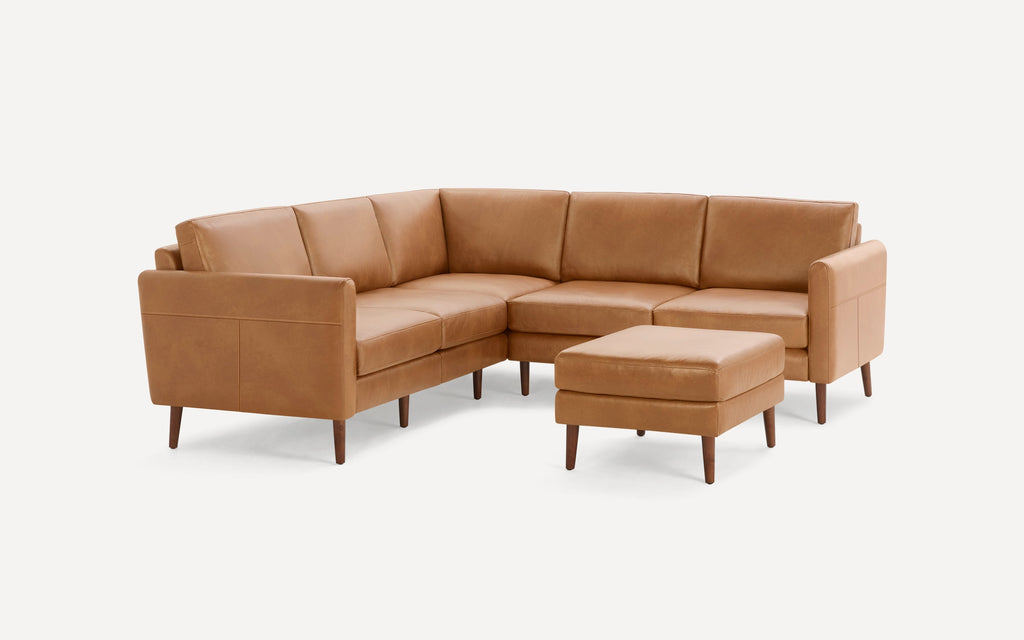 Mid-century modern tan leather sectional sofa with wooden legs and matching square ottoman on white background.