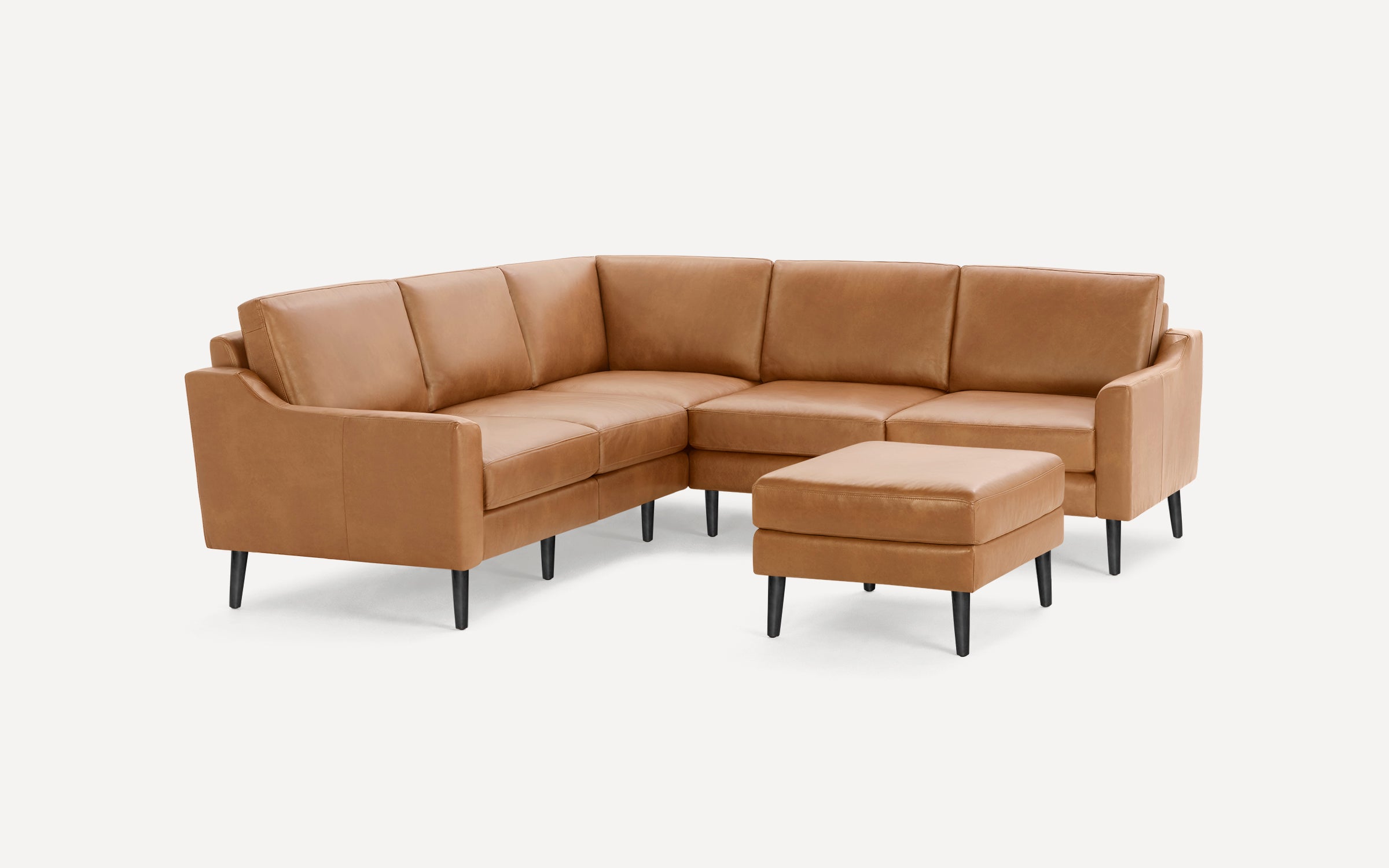 Modern tan leather L-shaped sectional sofa with matching ottoman and black tapered legs on a white background.