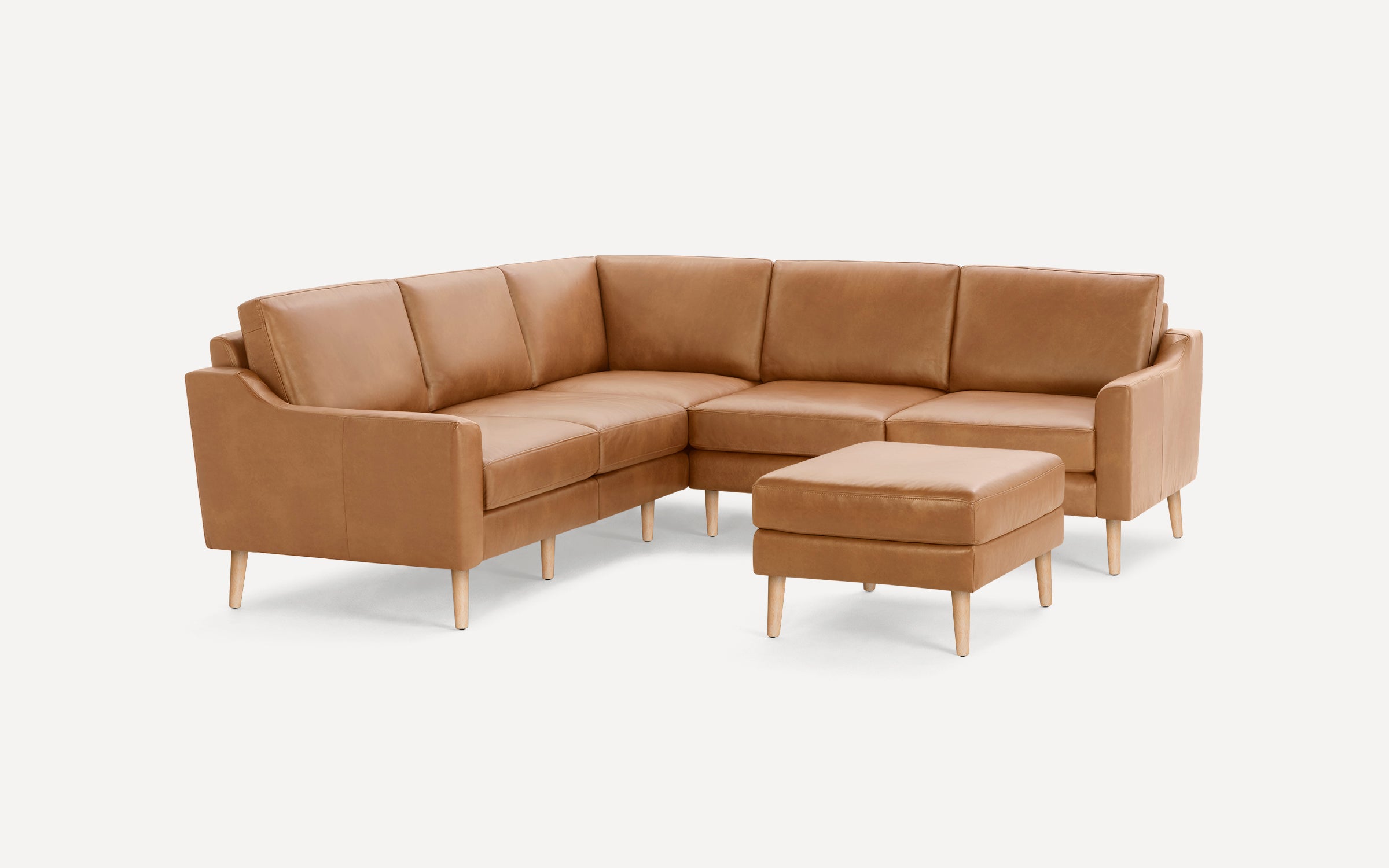 Tan leather L-shaped sectional sofa with wooden legs and matching square ottoman, isolated on white background.