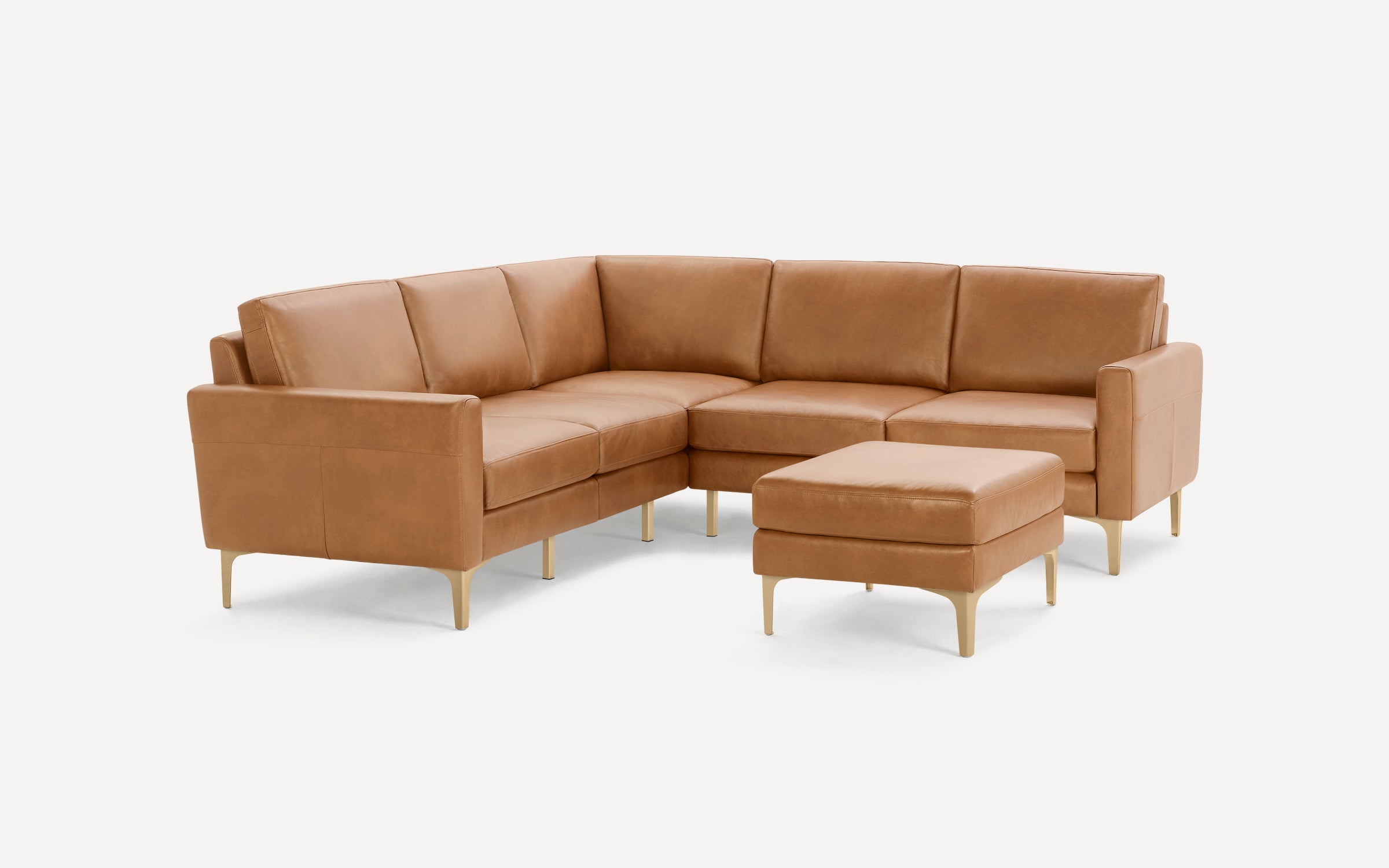 Modern camel brown leather sectional sofa with matching ottoman on light wooden legs, featured on plain white background.