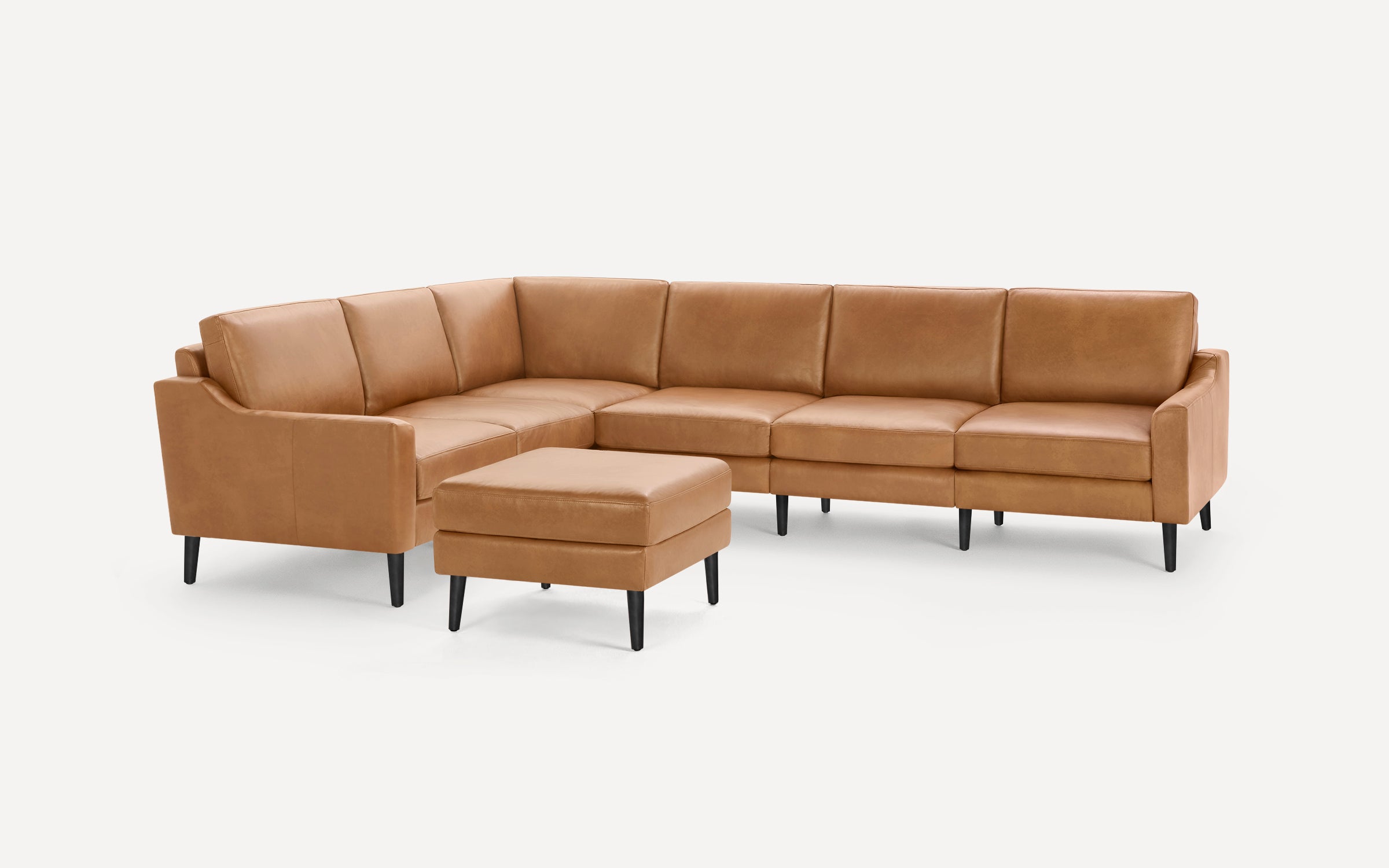 Modern L-shaped sectional sofa with tan leather upholstery and black tapered legs, including a matching ottoman.