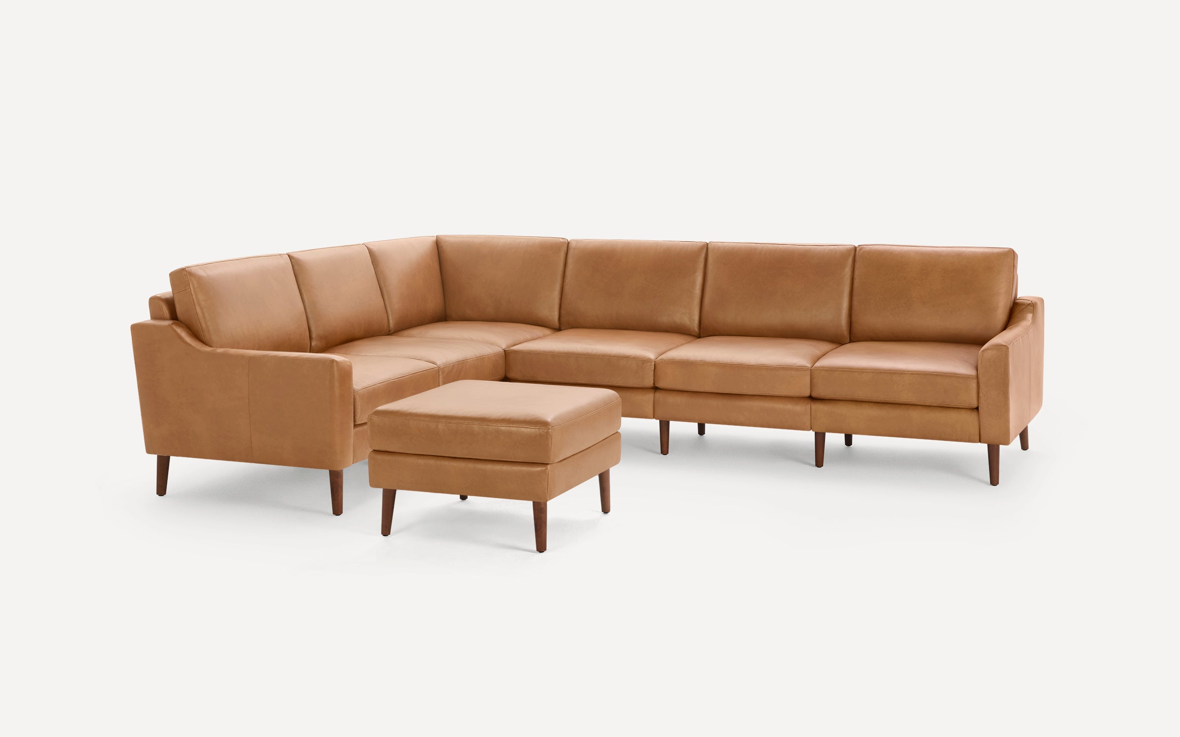 Modern mid-century style L-shaped tan leather sectional sofa with wooden legs and matching ottoman.