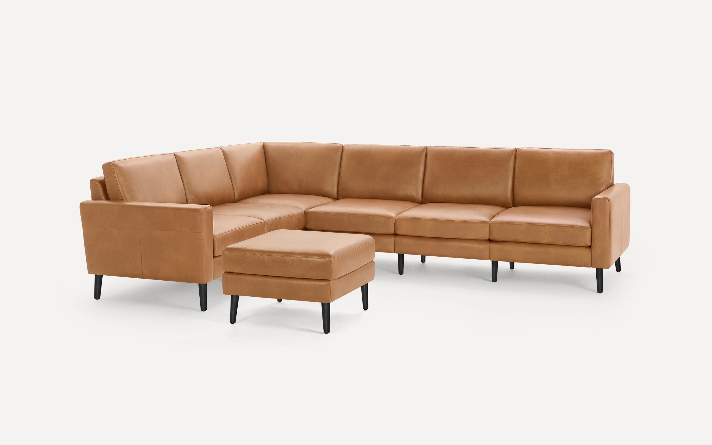 Modern tan leather sectional sofa with black tapered legs and matching square ottoman on white background.