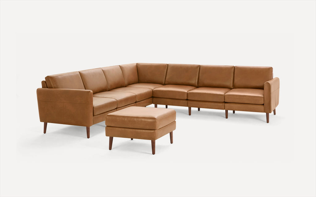 Mid-century modern tan leather sectional sofa with wooden legs and matching ottoman on white background.
