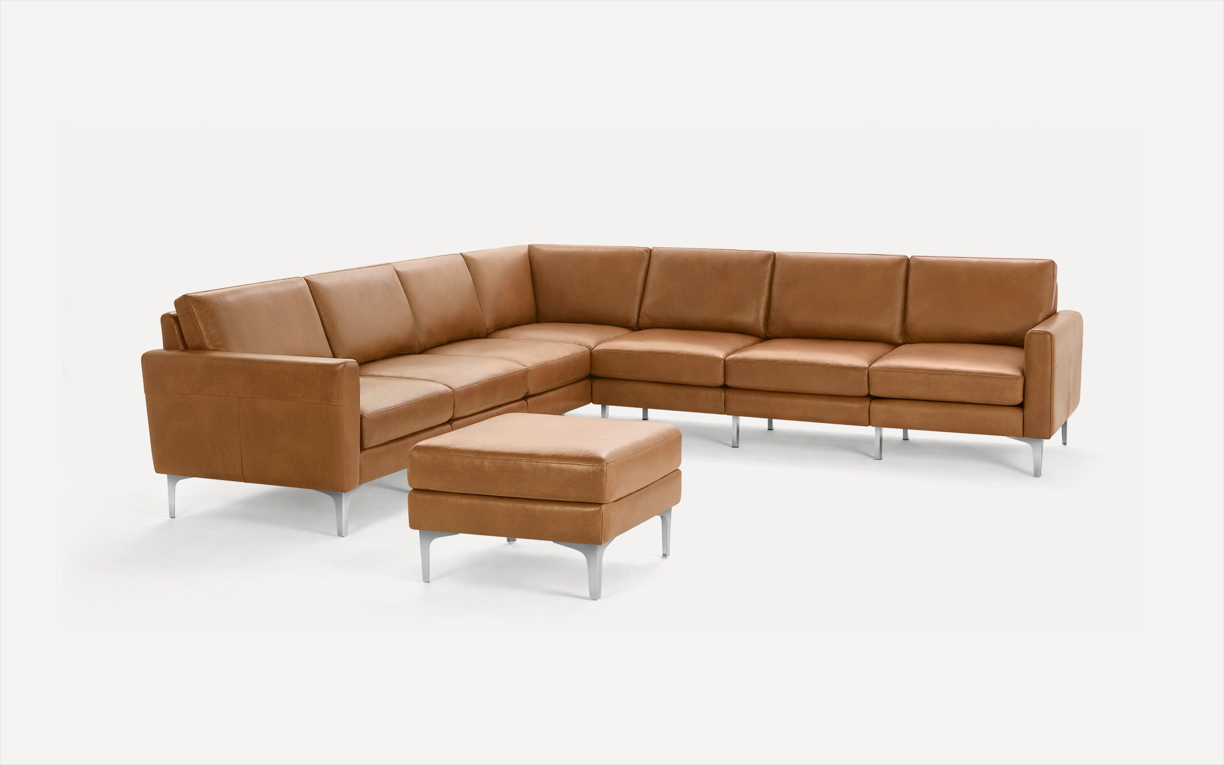 Modern L-shaped sectional sofa and matching ottoman in tan leather with metal legs on white background.