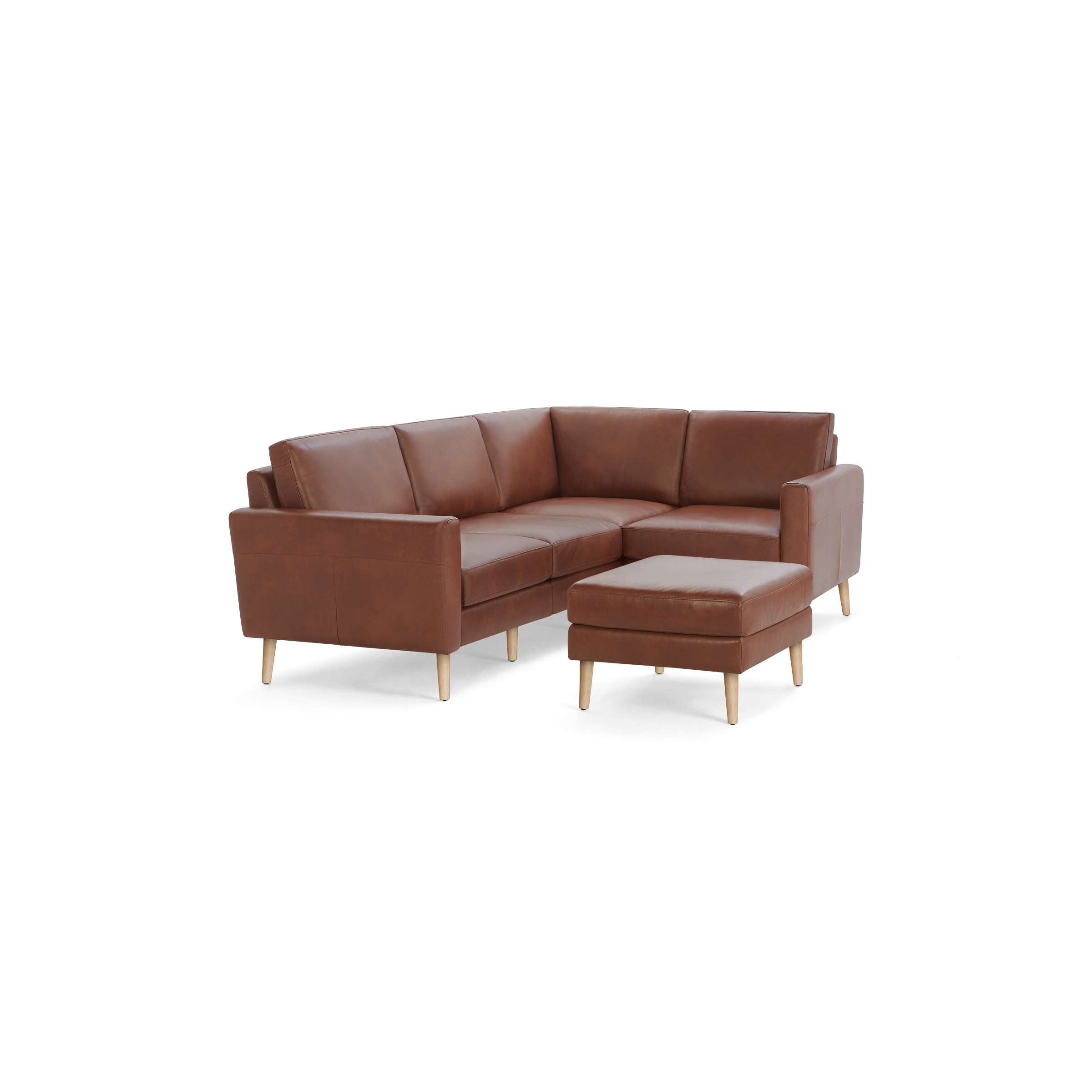 Brown leather L-shaped sectional sofa with wooden legs and matching ottoman on black background.