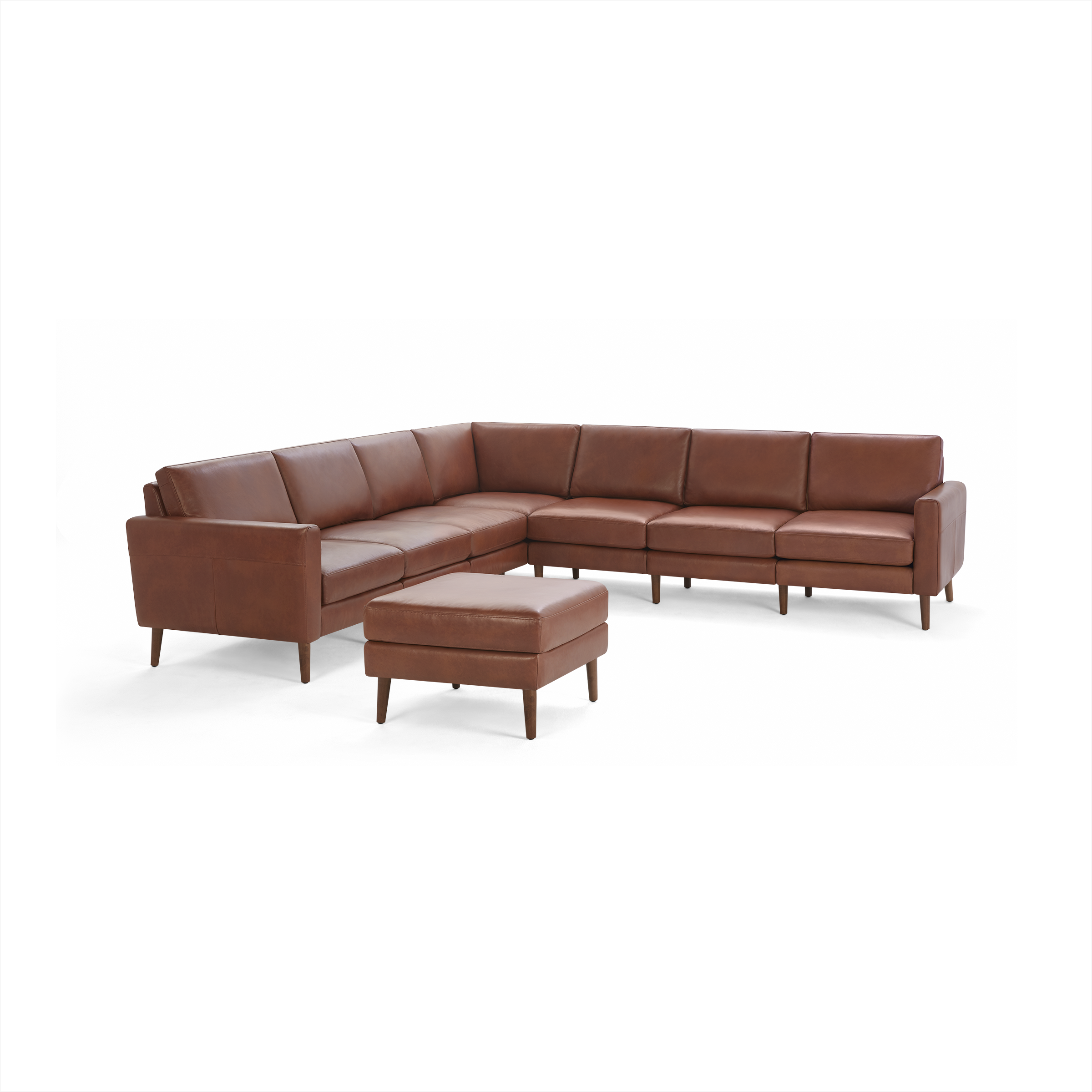 Modern L-shaped sectional sofa and matching ottoman in warm brown leather with wooden legs, designed for spacious living rooms.
