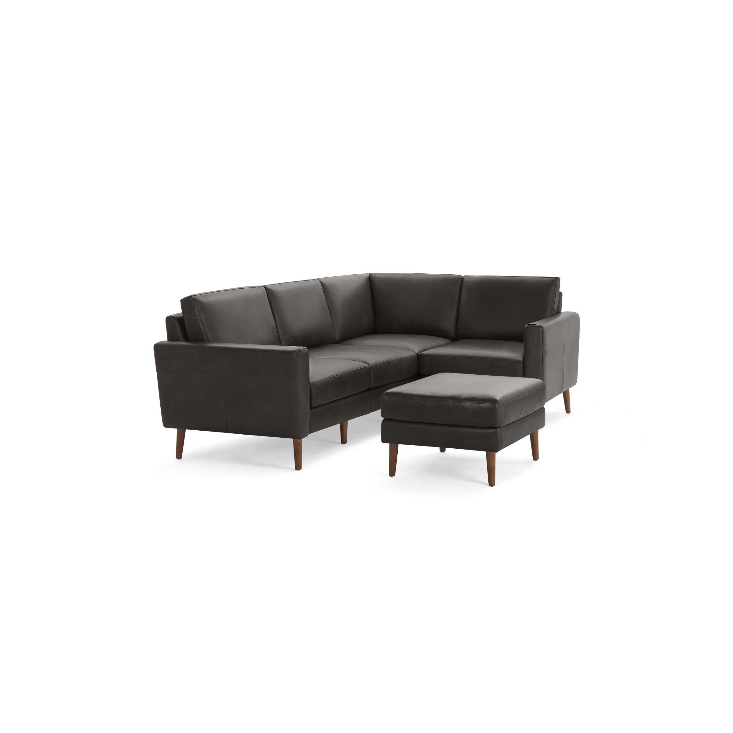 Dark gray leather L-shaped sectional sofa with wooden legs and matching ottoman against black background.