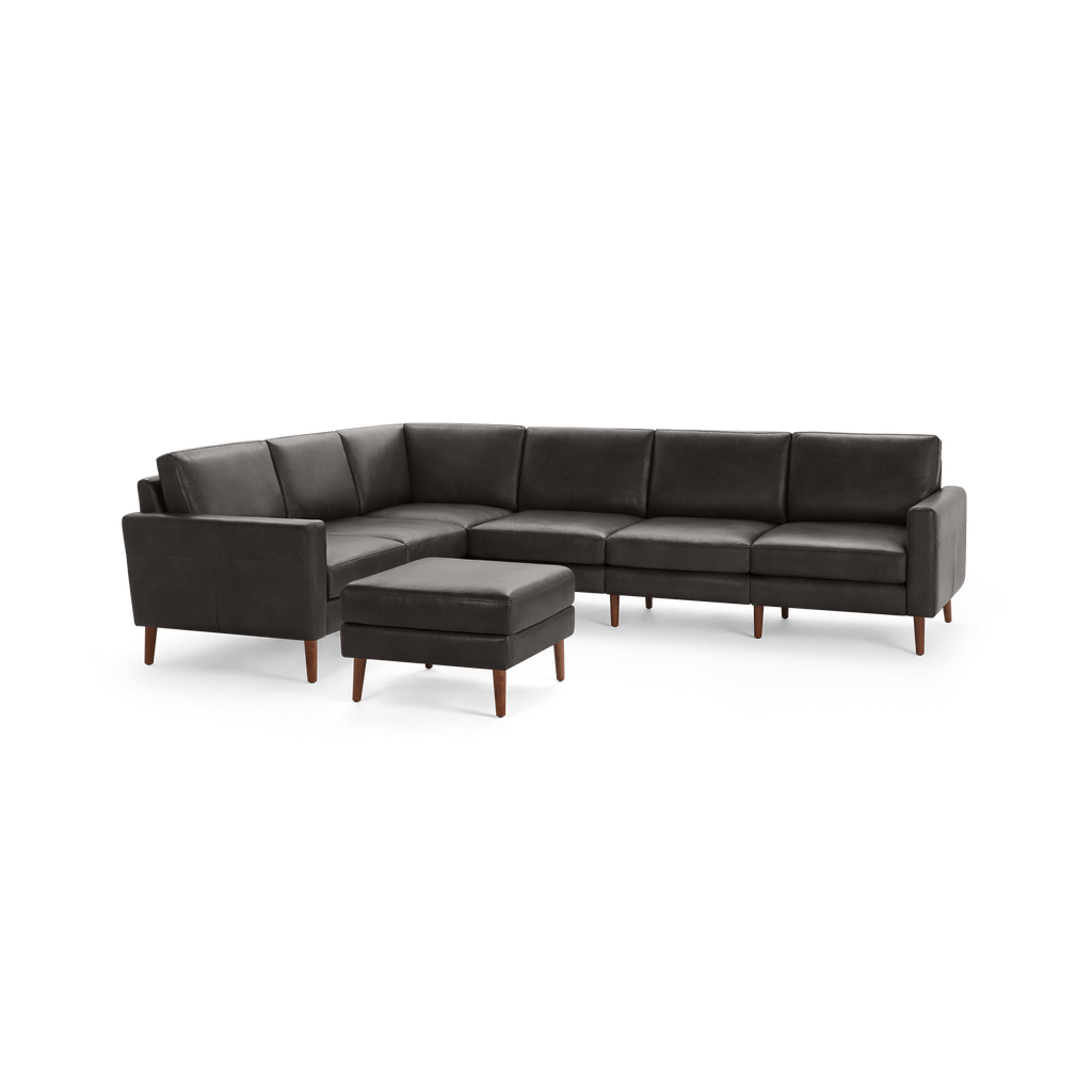 Dark gray leather L-shaped sectional sofa with wooden legs and matching square ottoman, modern, sleek design.