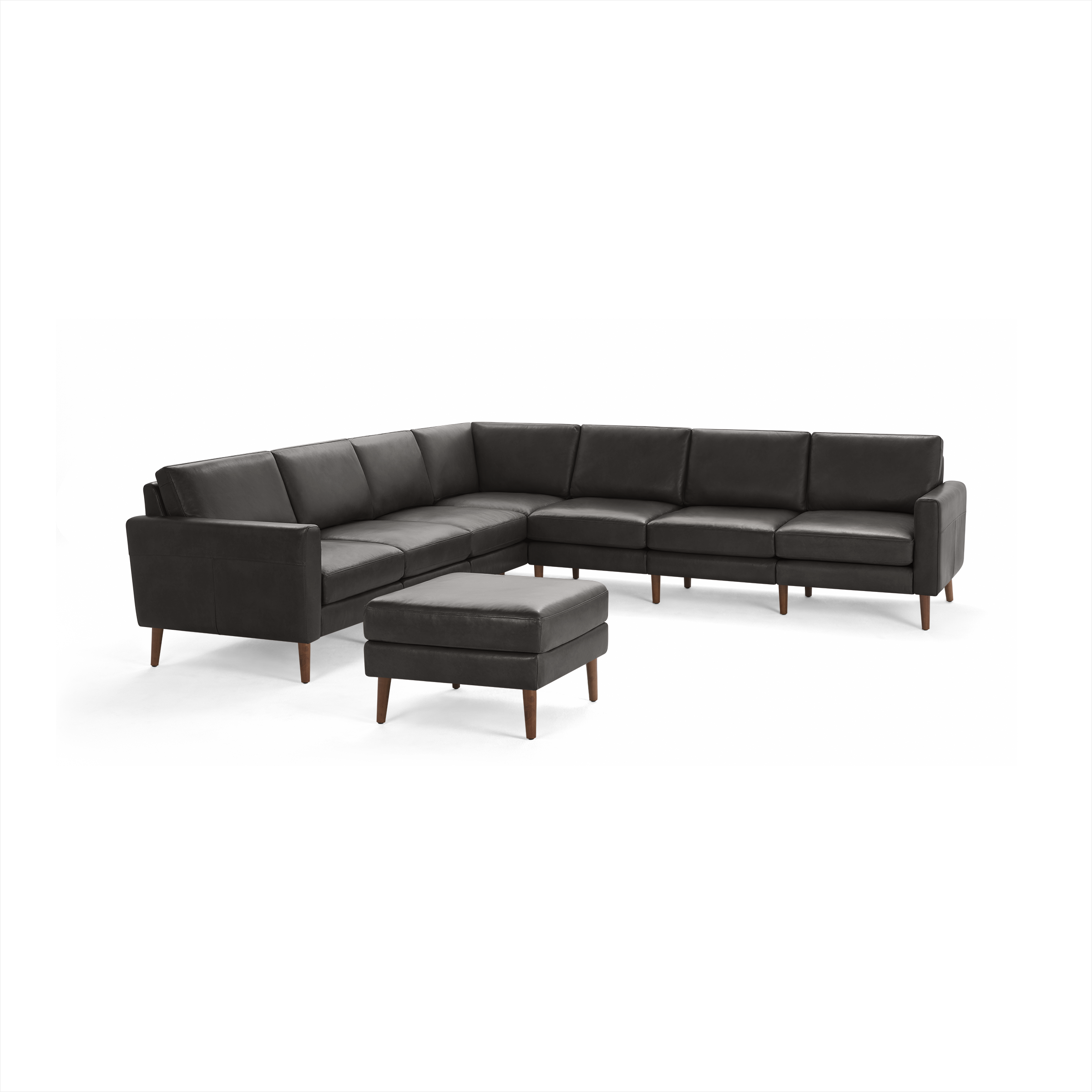 Dark grey leather sectional sofa with wooden legs and matching ottoman, modern L-shaped design.