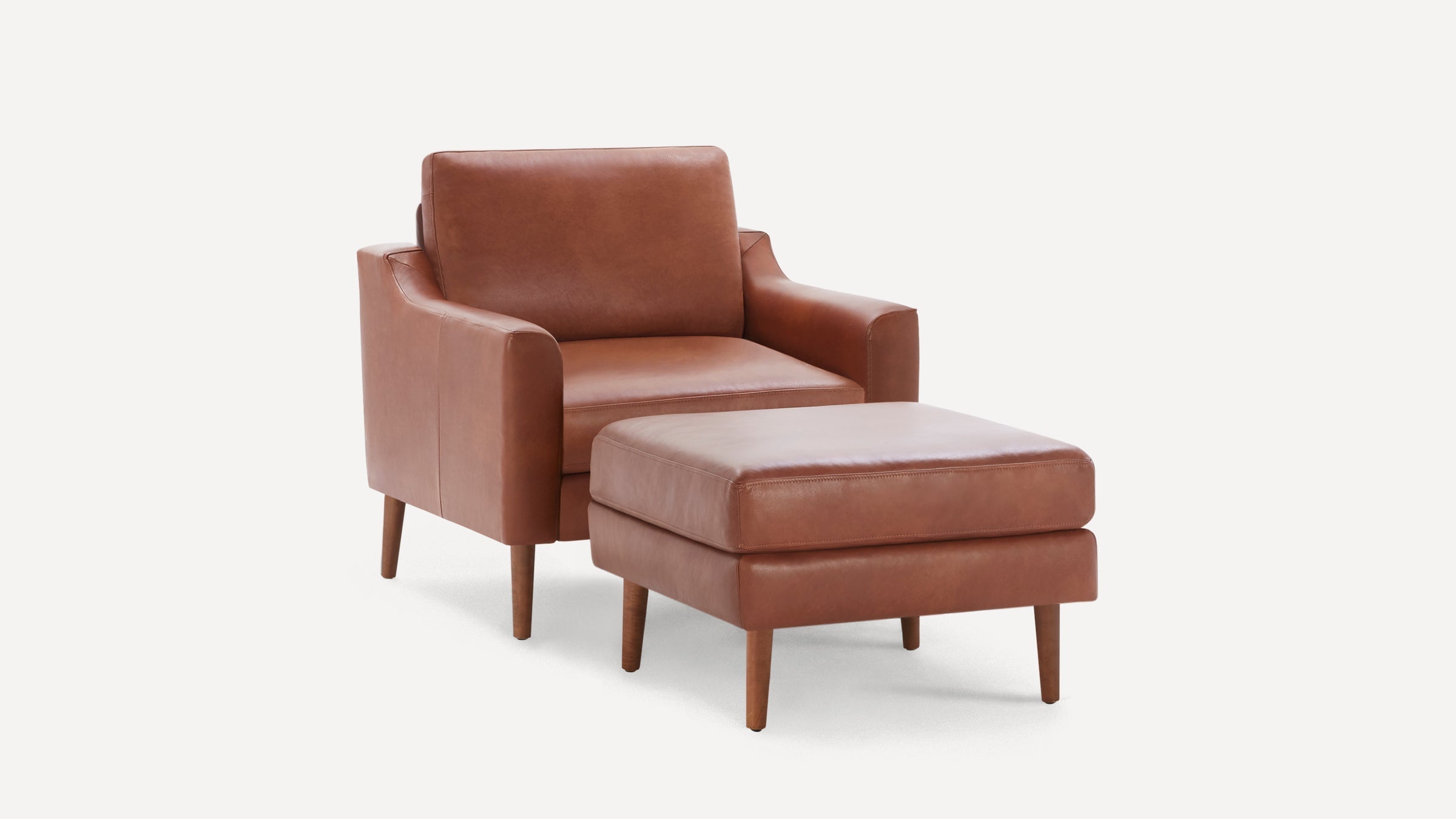 Brown leather armchair with matching ottoman, both featuring wooden legs and modern, sleek design on white background.