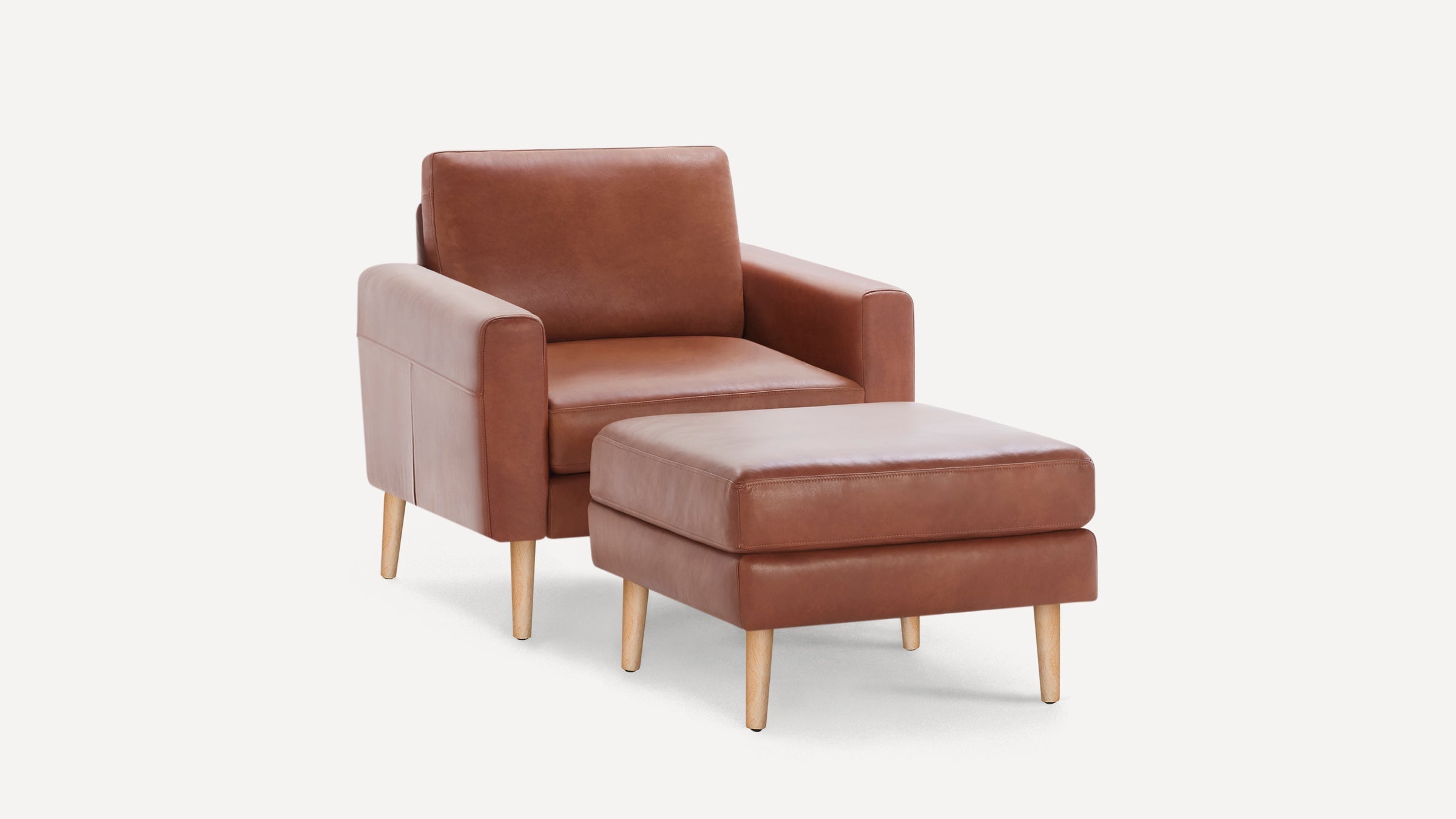 Mid-century style brown leather armchair with matching ottoman, both featuring light wooden legs, on white background.