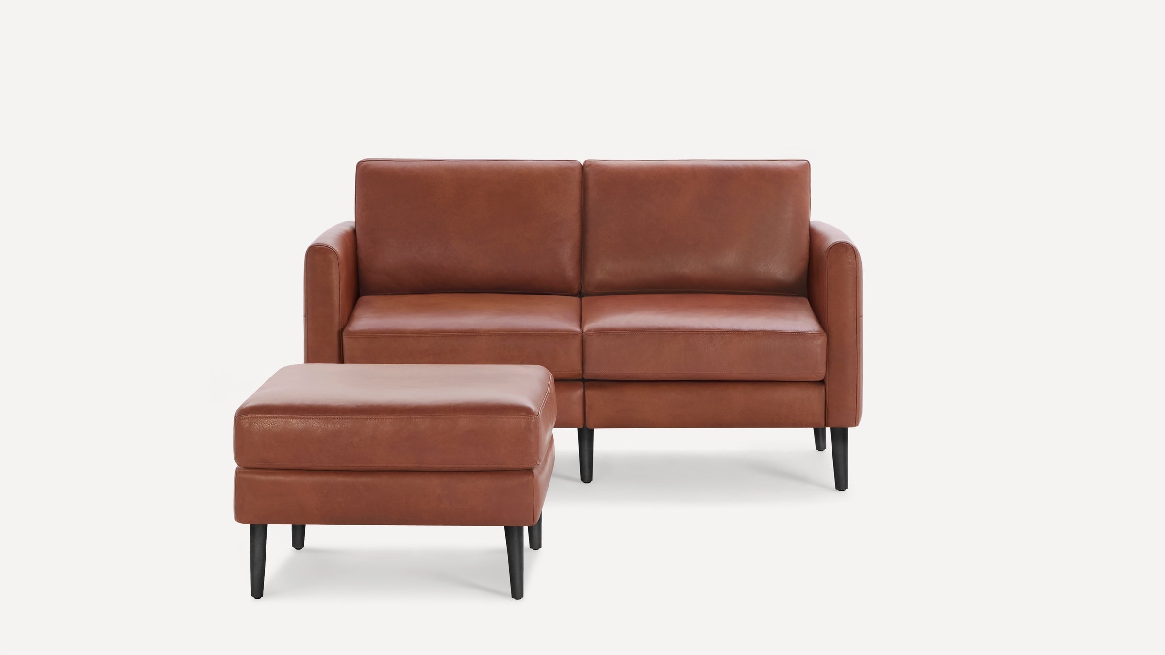Brown leather loveseat sofa with matching ottoman, featuring clean lines and black tapered legs on white background.