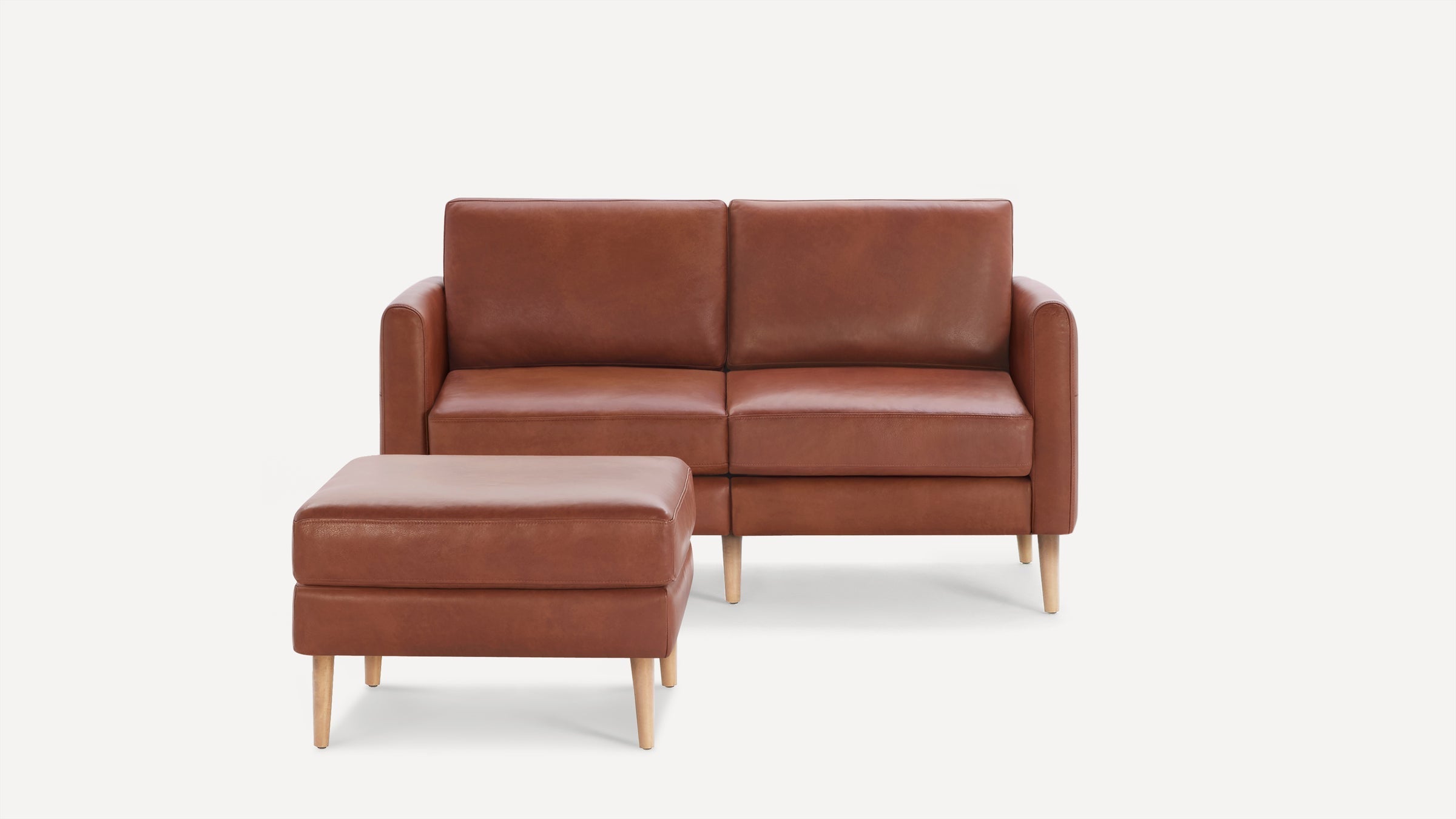 Brown leather two-seater sofa with matching ottoman, both featuring light wooden legs on a white background.
