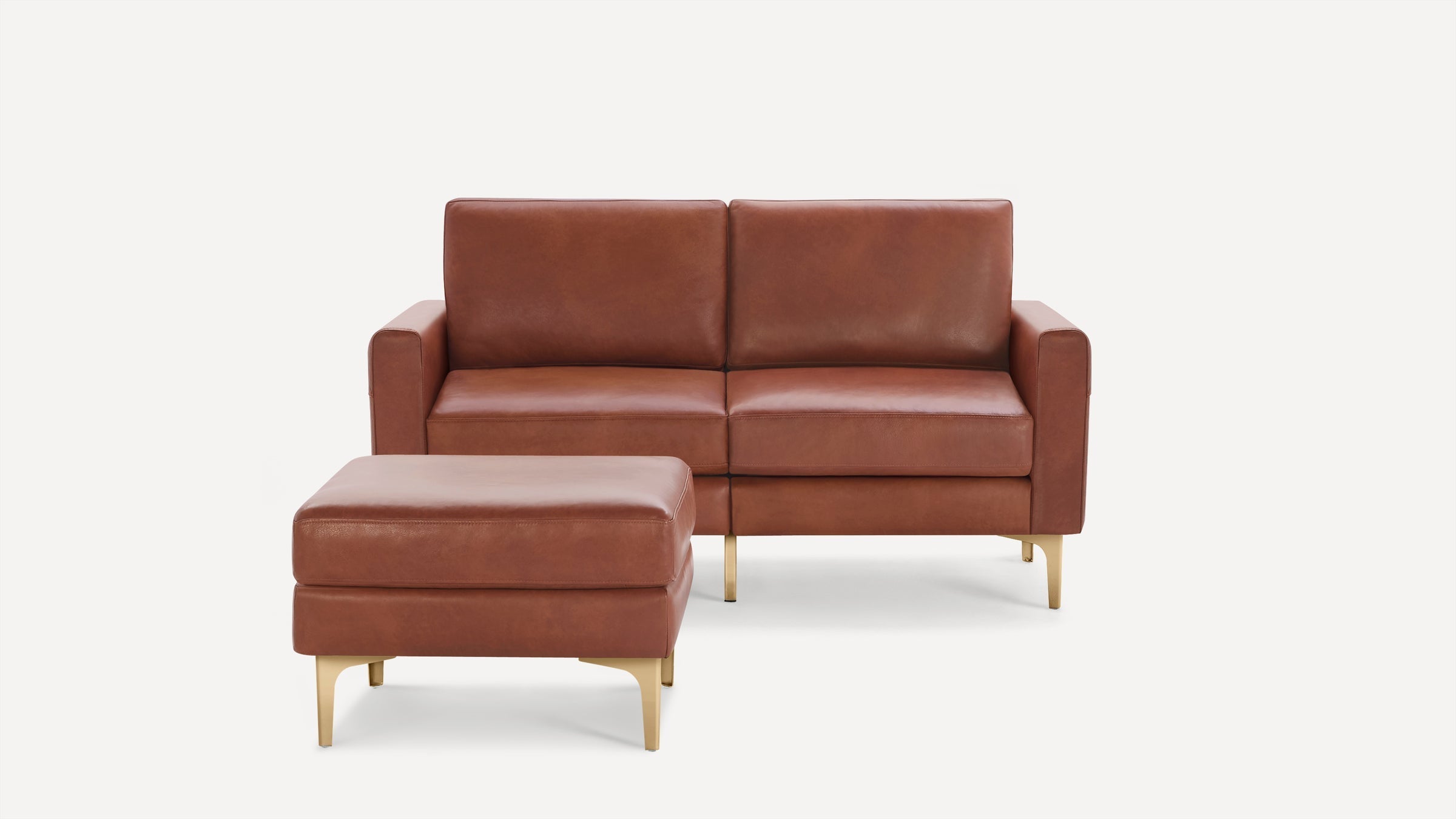 Mid-century modern two-seater sofa with matching ottoman in brown leather and gold metal legs, against a plain white background.