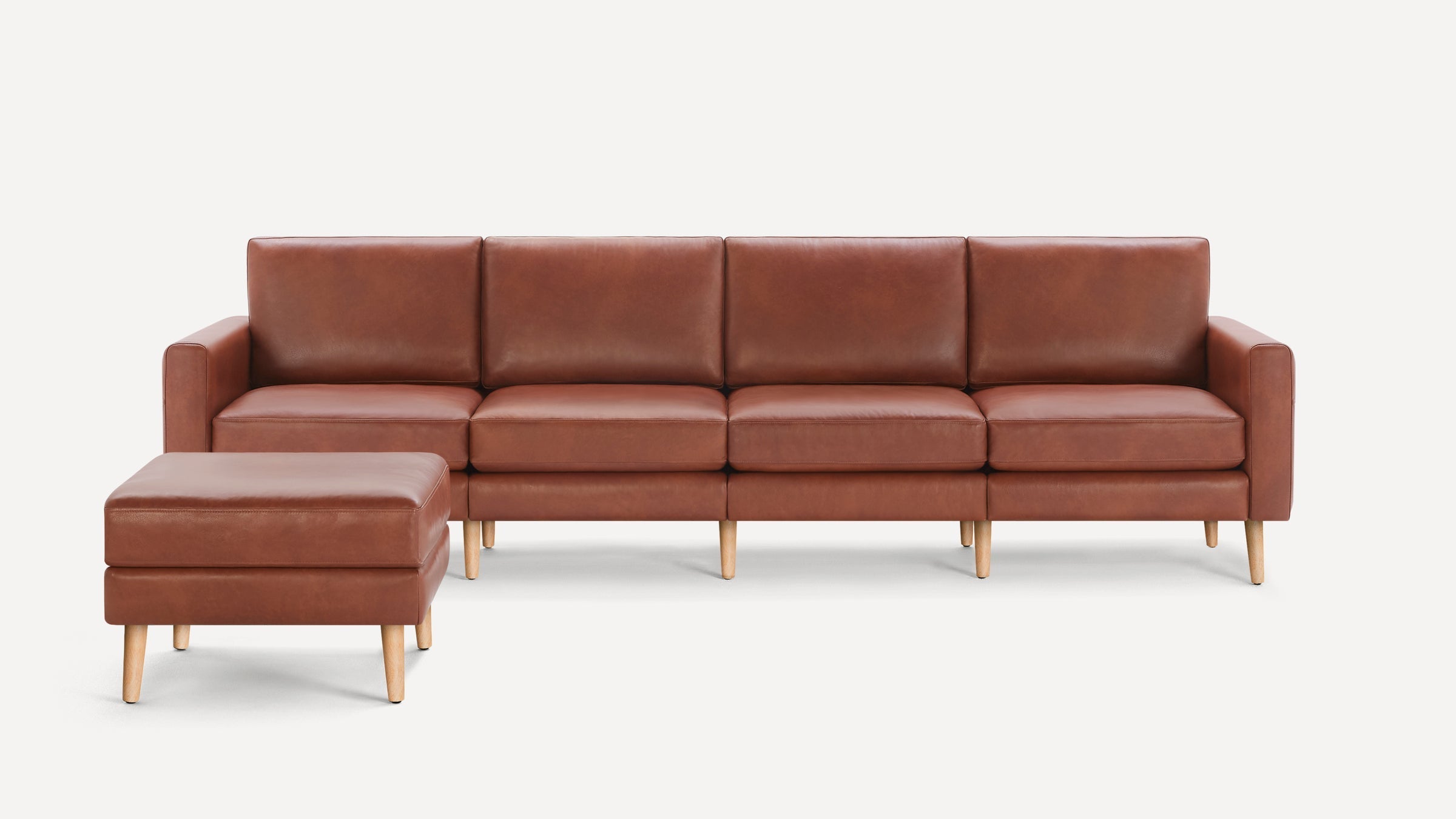 Brown leather sectional sofa with matching ottoman, featuring clean lines and wooden legs, on a white background.