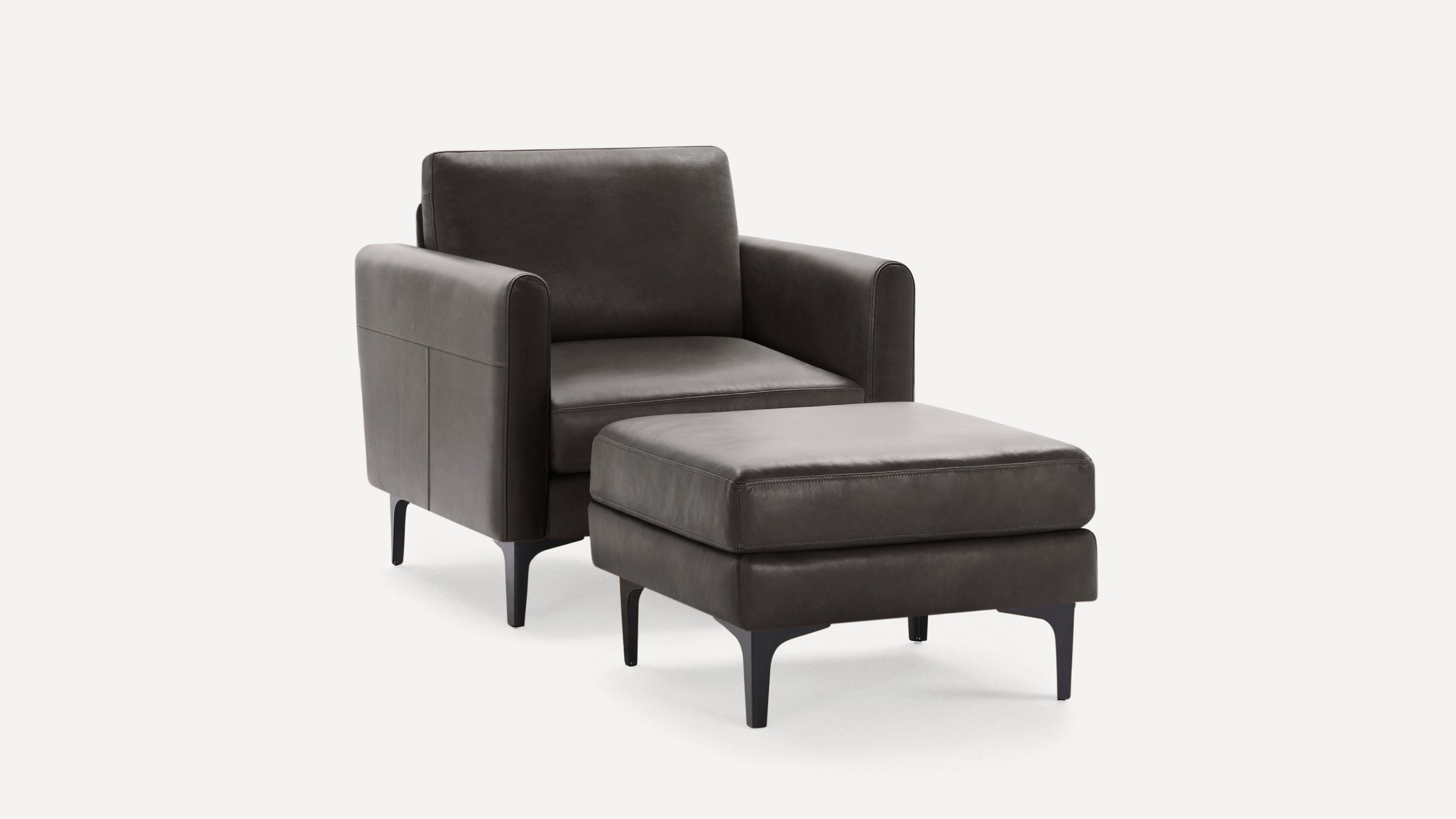 Dark gray leather armchair with matching ottoman, both featuring slim black legs and modern, minimalist design.