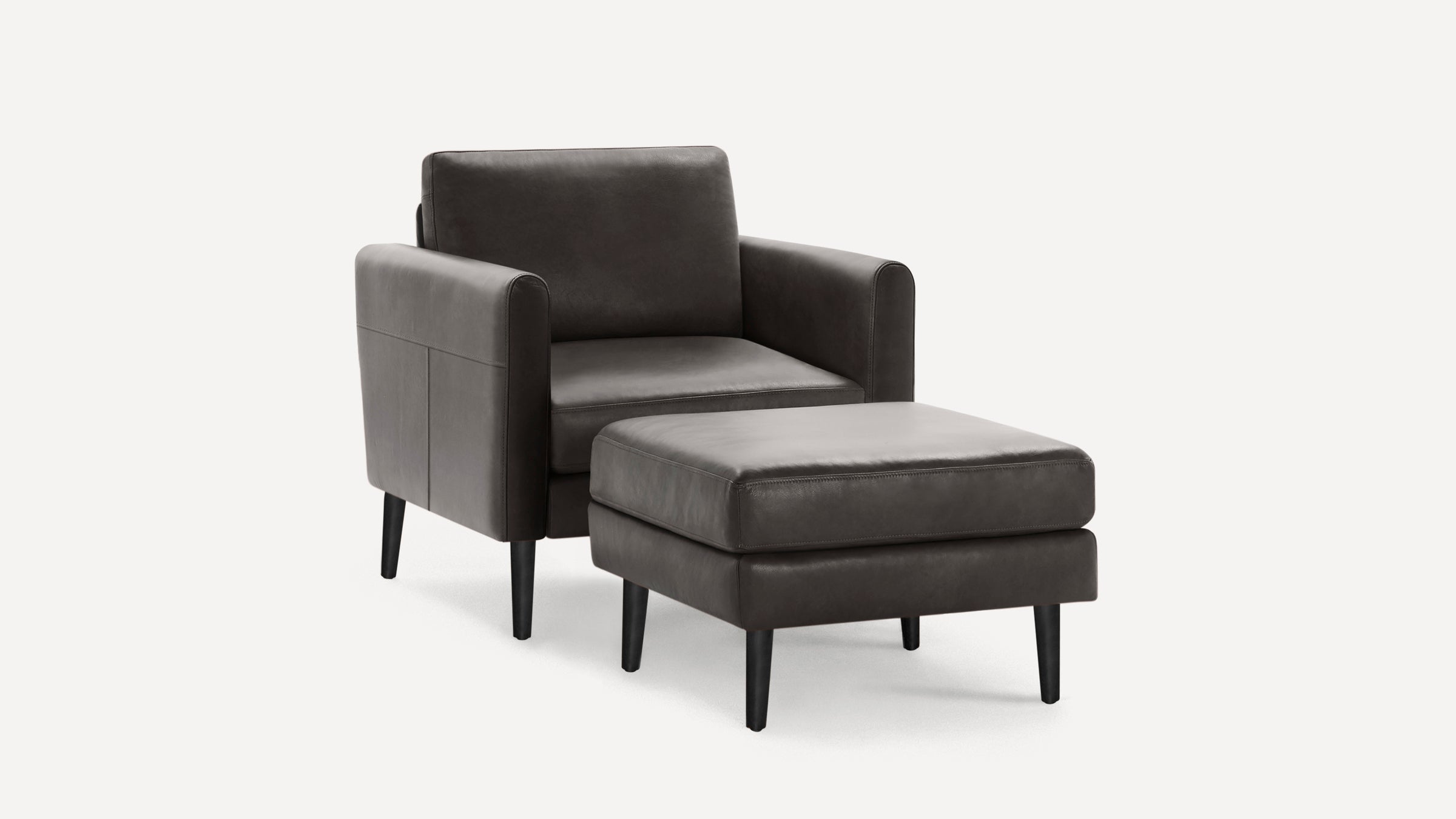 Modern dark gray leather armchair with matching ottoman, sleek black legs, and clean, minimalist design.