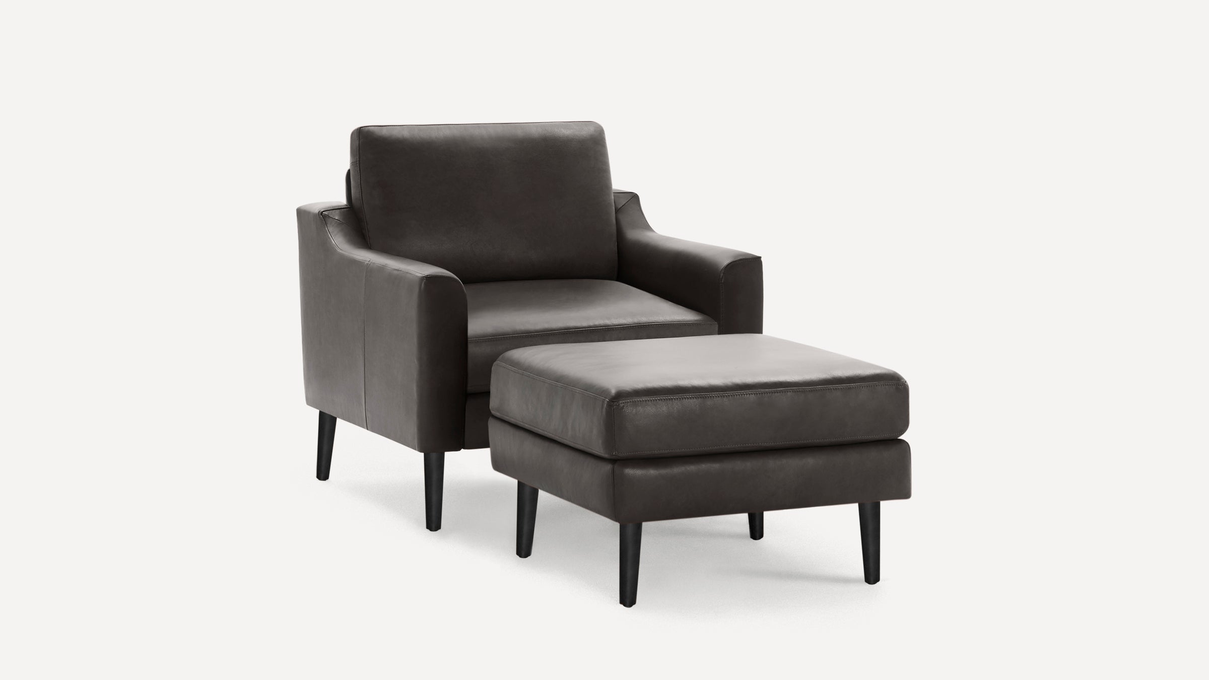 Dark gray leather armchair with matching ottoman, both featuring black tapered legs and a modern, sleek design.
