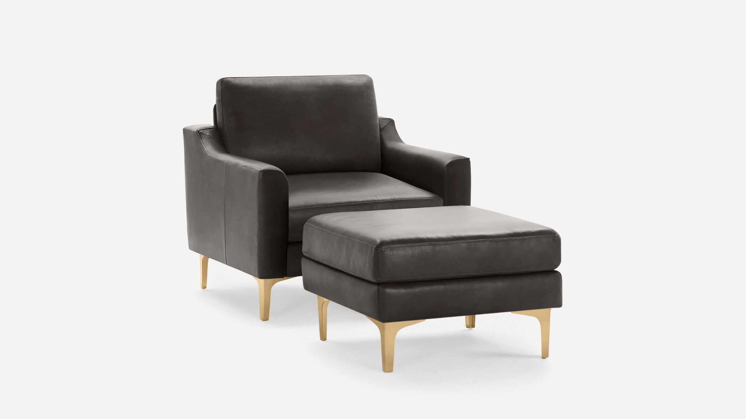 Dark gray leather armchair with matching ottoman, both featuring sleek gold metal legs, set against a white background.