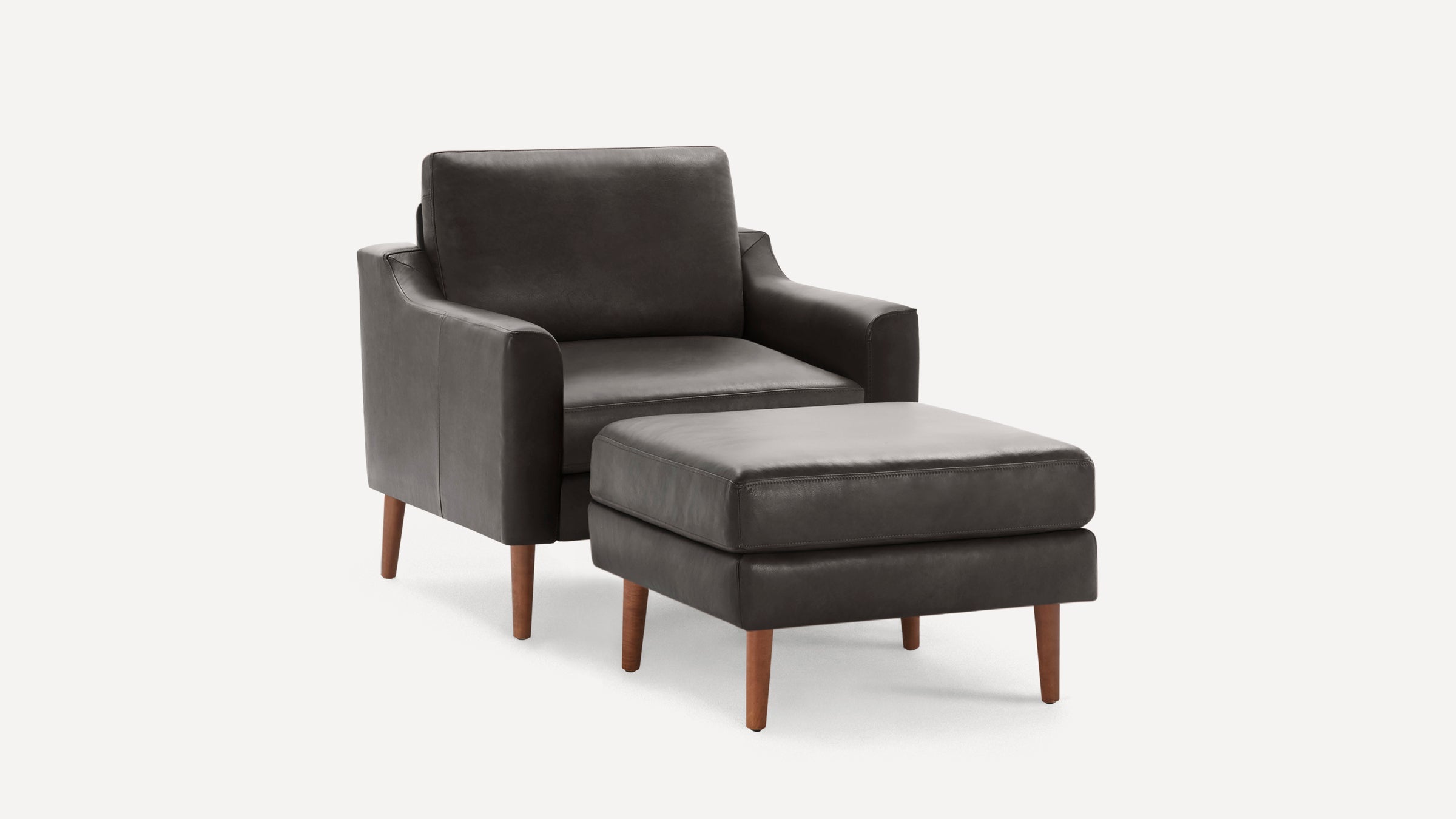 Dark gray leather armchair with matching ottoman, both featuring wooden tapered legs and minimalist modern design.