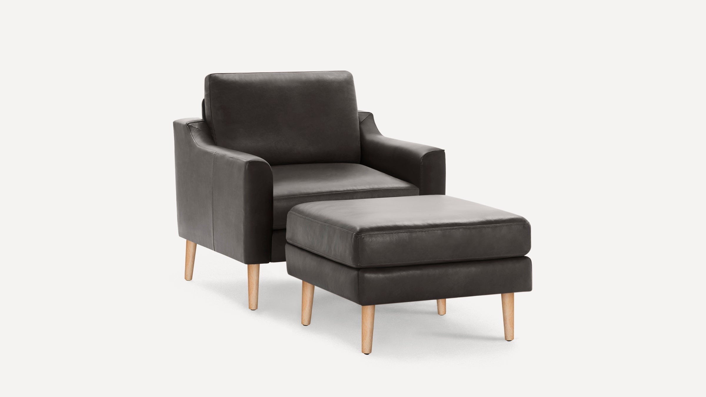Modern dark gray leather armchair with matching square ottoman and light wooden legs on a white background.