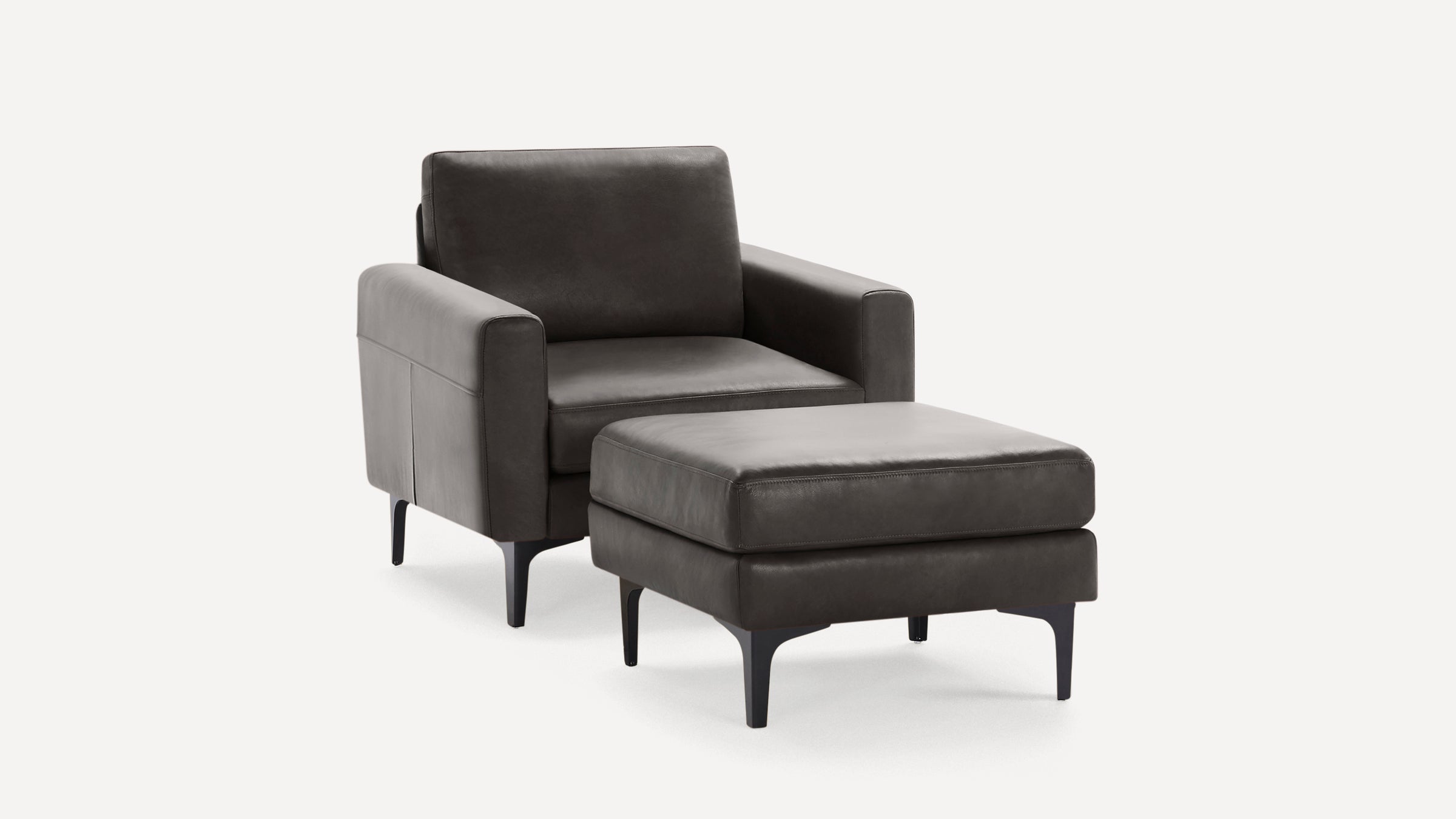 Dark gray leather armchair with matching ottoman, both featuring slim black legs and modern, minimalist design.
