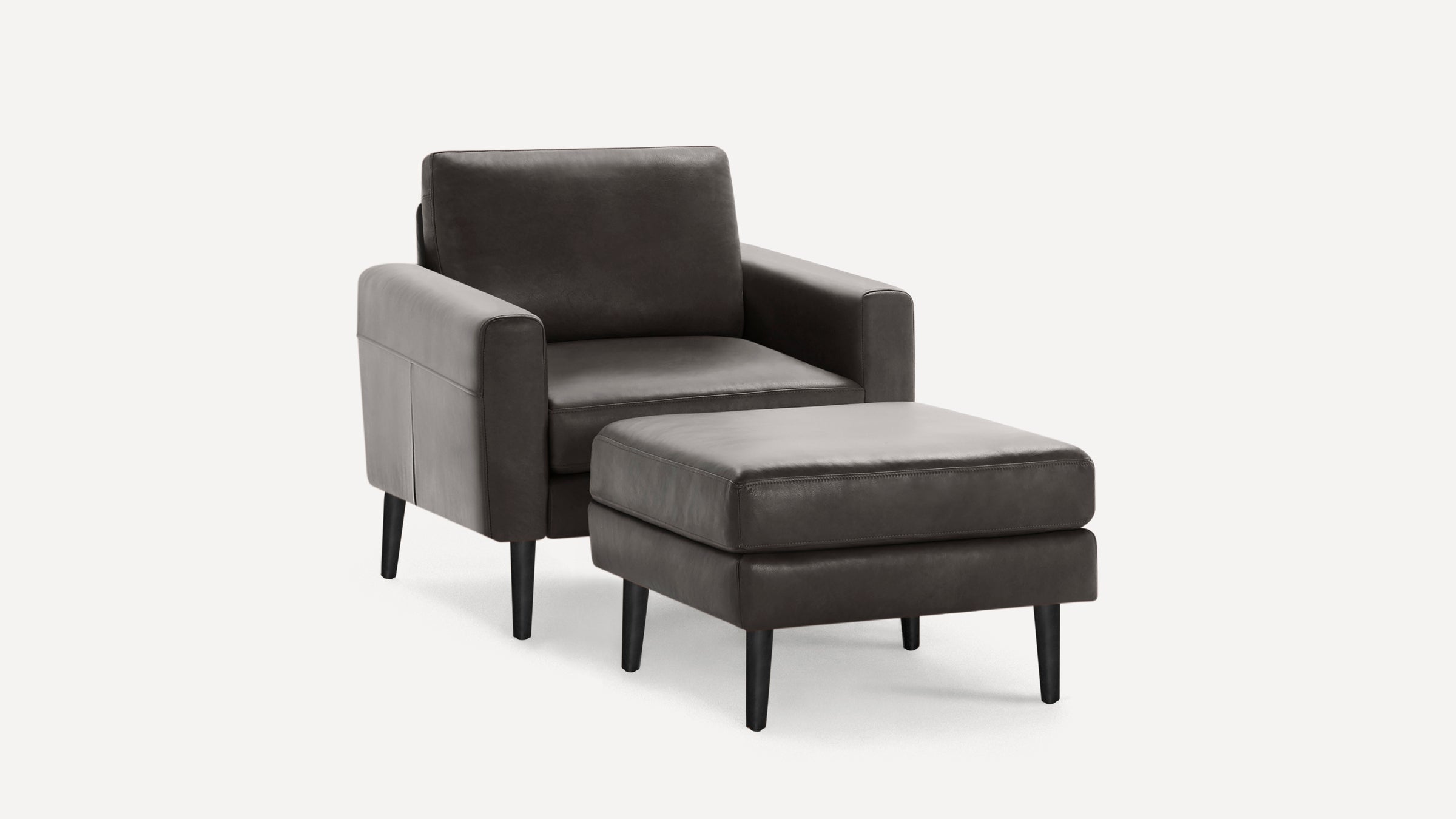 Dark gray modern leather armchair with matching ottoman, featuring clean lines and black tapered legs on a white background.
