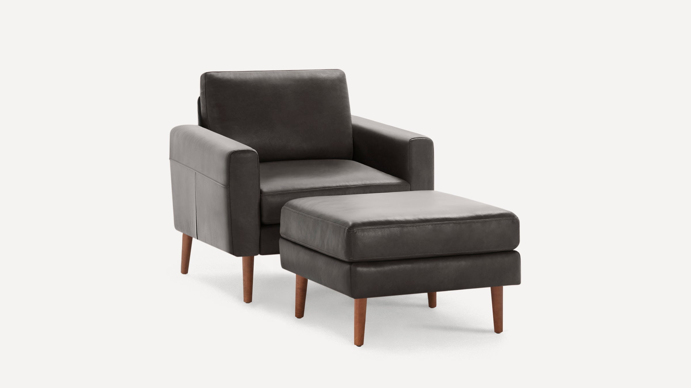 Modern dark gray leather armchair with matching ottoman, featuring clean lines and wooden tapered legs on a white background.