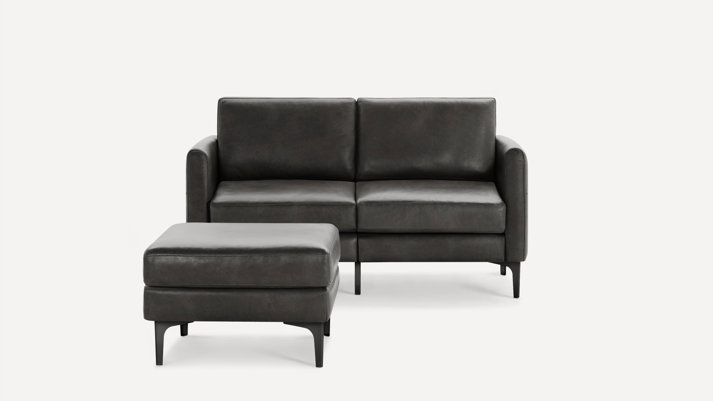 Modern dark gray leather loveseat sofa with matching ottoman, sleek metal legs, and clean lines against a white background.