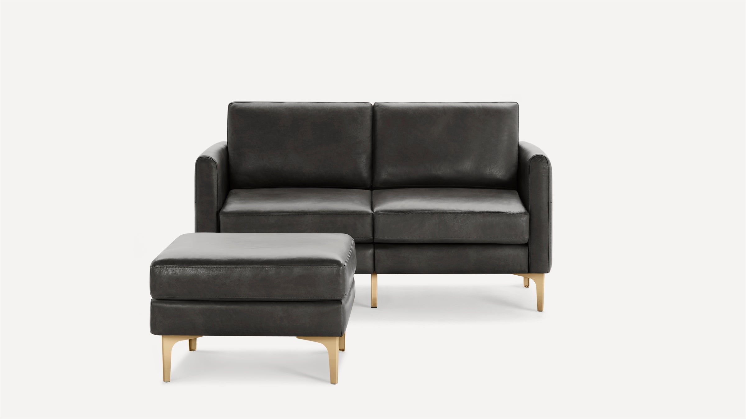 Dark gray leather loveseat with matching ottoman, both featuring gold-toned metal legs and modern, clean lines.