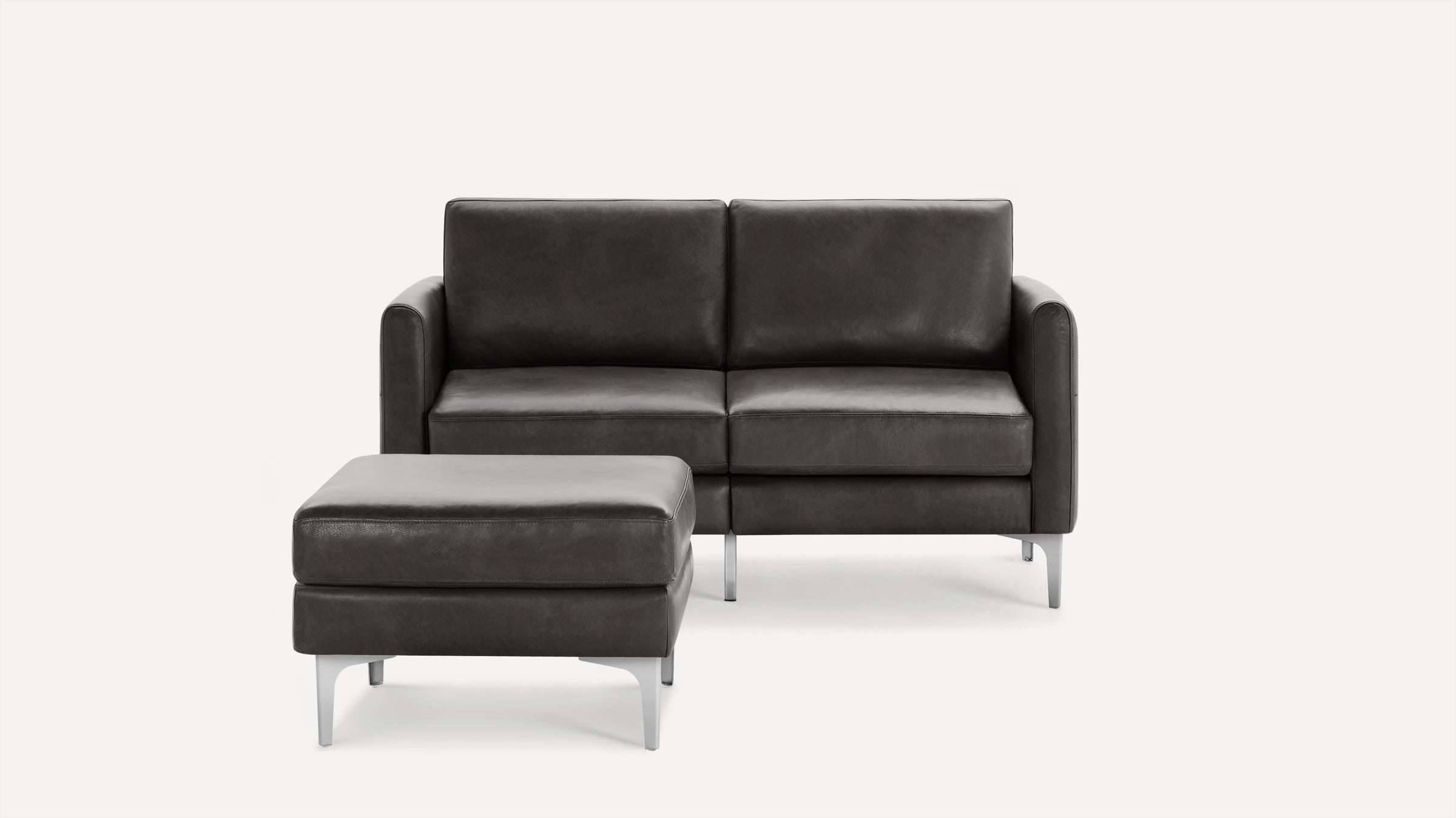 Dark gray leather loveseat sofa with matching ottoman, both featuring sleek metal legs and clean modern design.