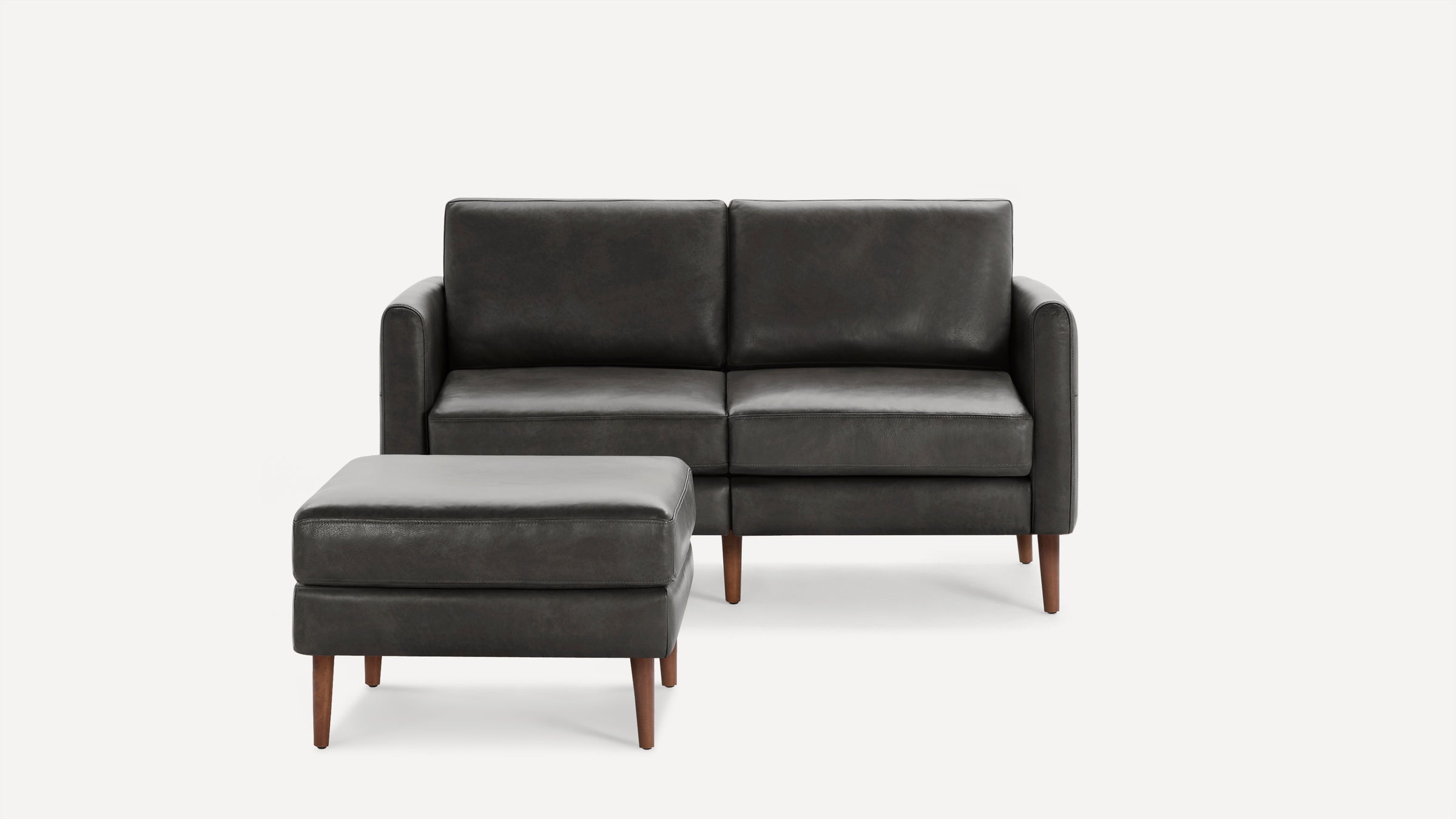 Dark gray leather two-seater sofa with matching ottoman, featuring wooden legs and clean, modern design.