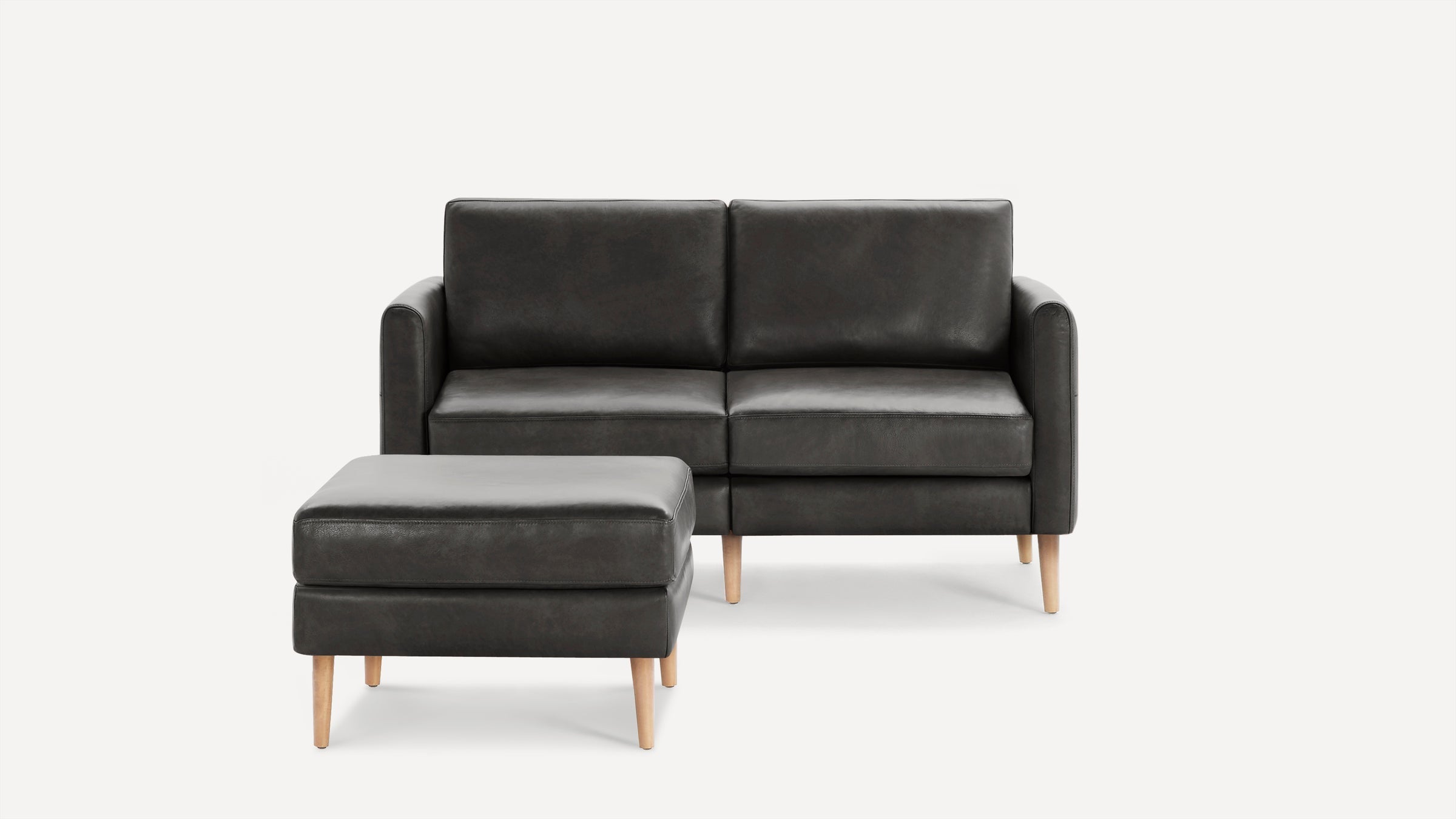 Dark gray modern loveseat sofa with matching ottoman, featuring smooth leather upholstery and light wooden legs.