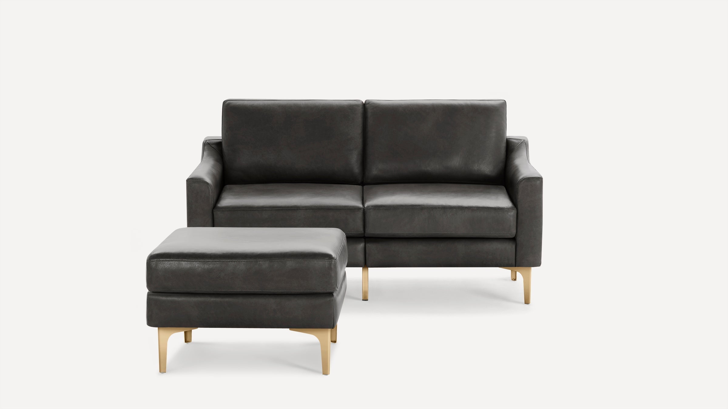 Dark gray leather loveseat with matching ottoman and gold metal legs, set against a plain white background.