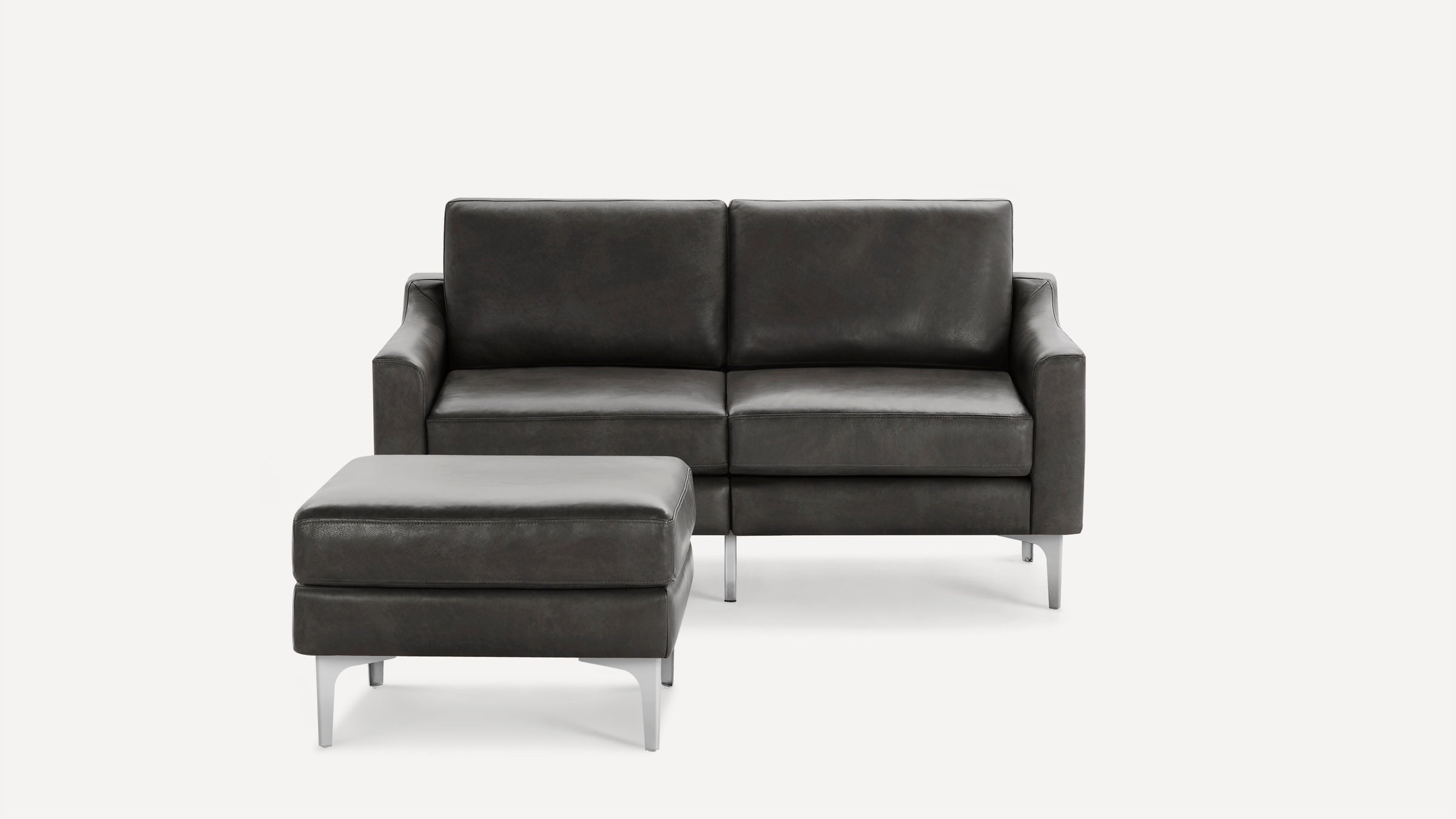 Modern dark gray leather loveseat sofa with matching ottoman, featuring sleek metal legs and minimalist design.