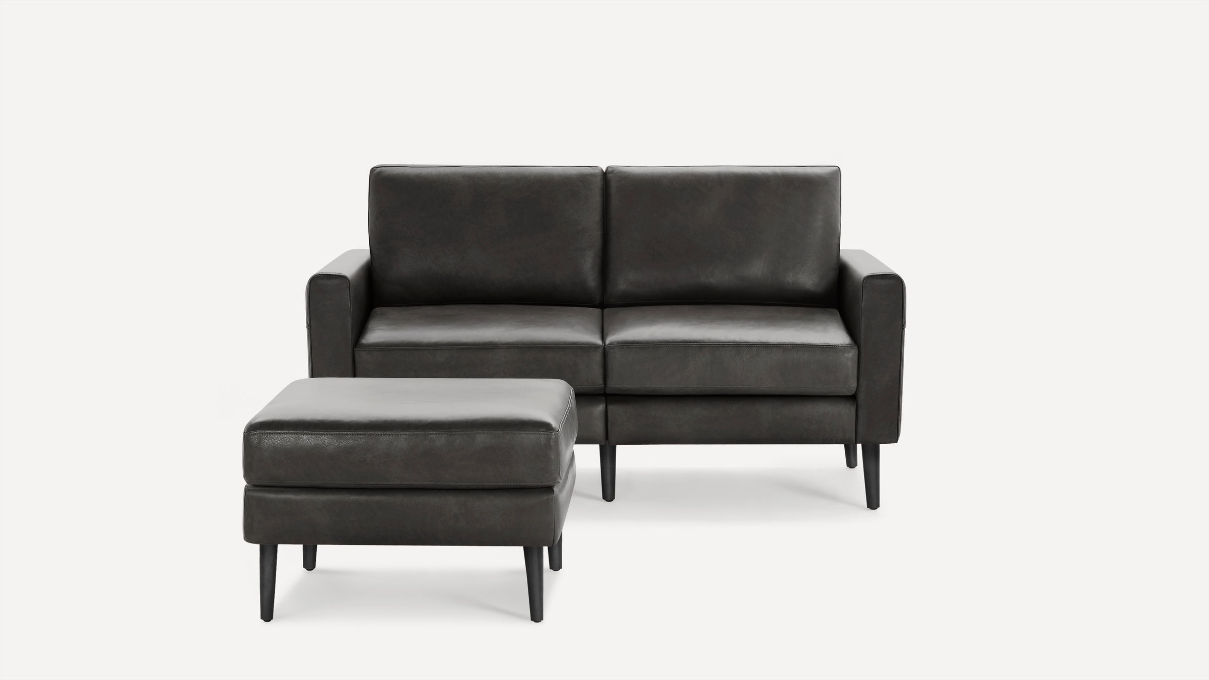 Dark gray leather loveseat with matching ottoman, featuring clean lines and black tapered wooden legs.