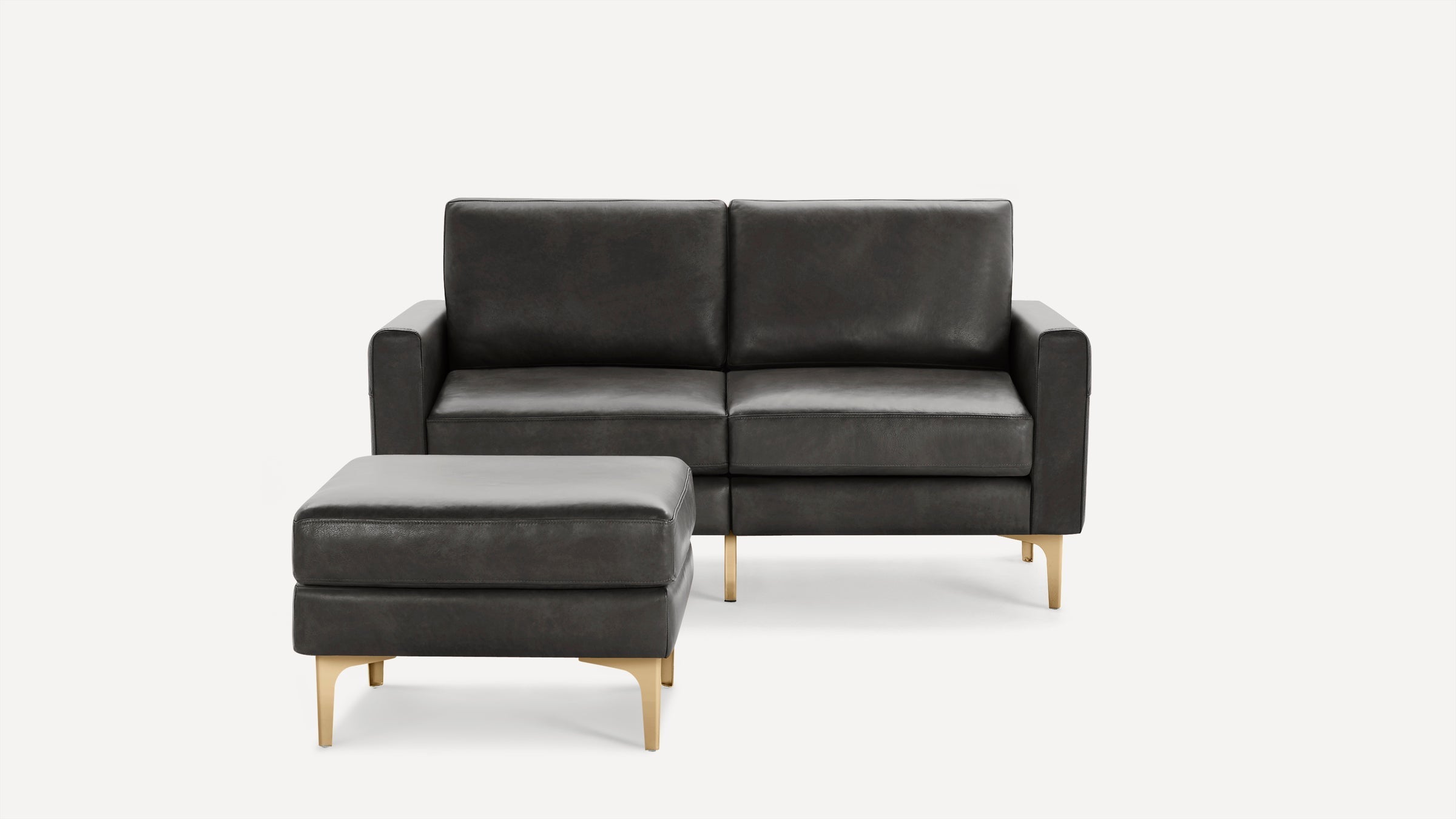 Modern dark gray leather loveseat with matching ottoman, both featuring sleek gold metal legs and clean lines.
