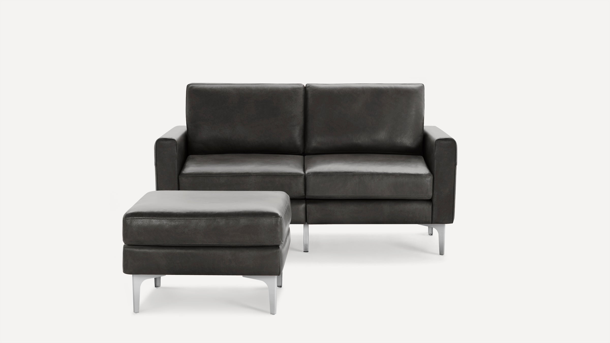Dark gray modern leather loveseat with matching ottoman, featuring sleek metal legs and clean, boxy design.