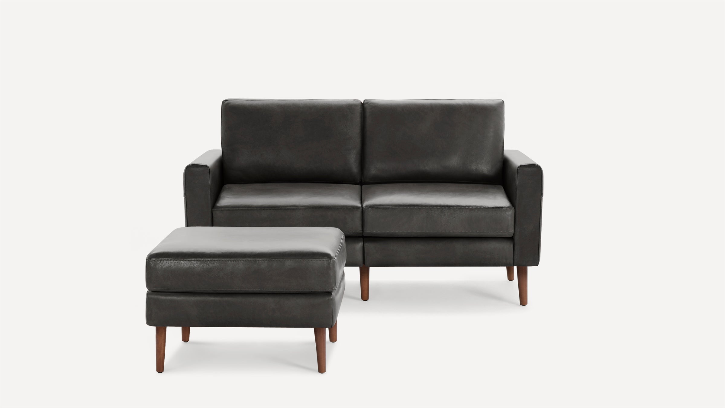 Modern dark gray leather loveseat with matching ottoman, both featuring wooden legs and clean, minimalist design.
