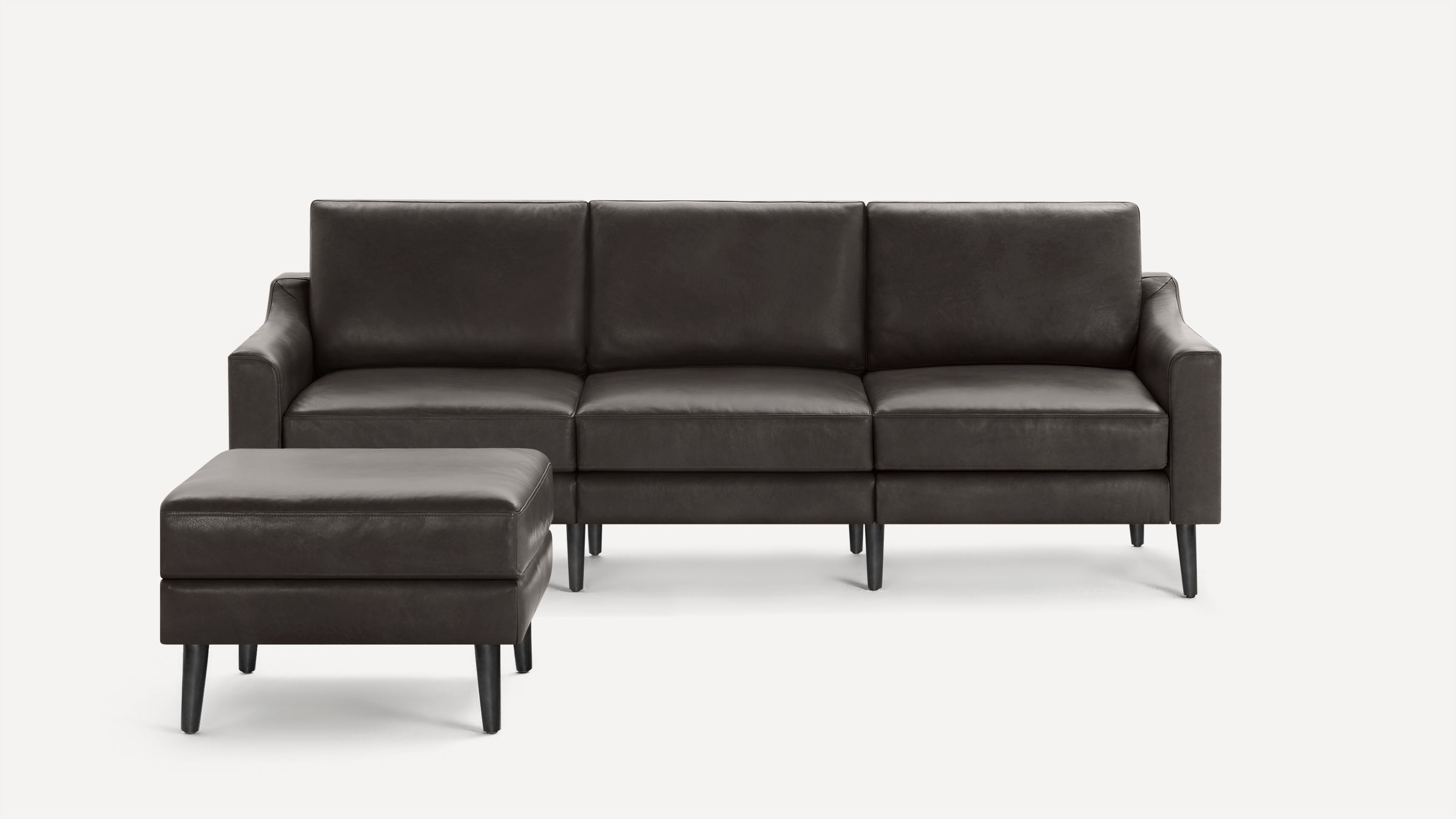 Dark brown leather three-seat sofa with matching ottoman, clean lines, and black tapered legs against a white background.
