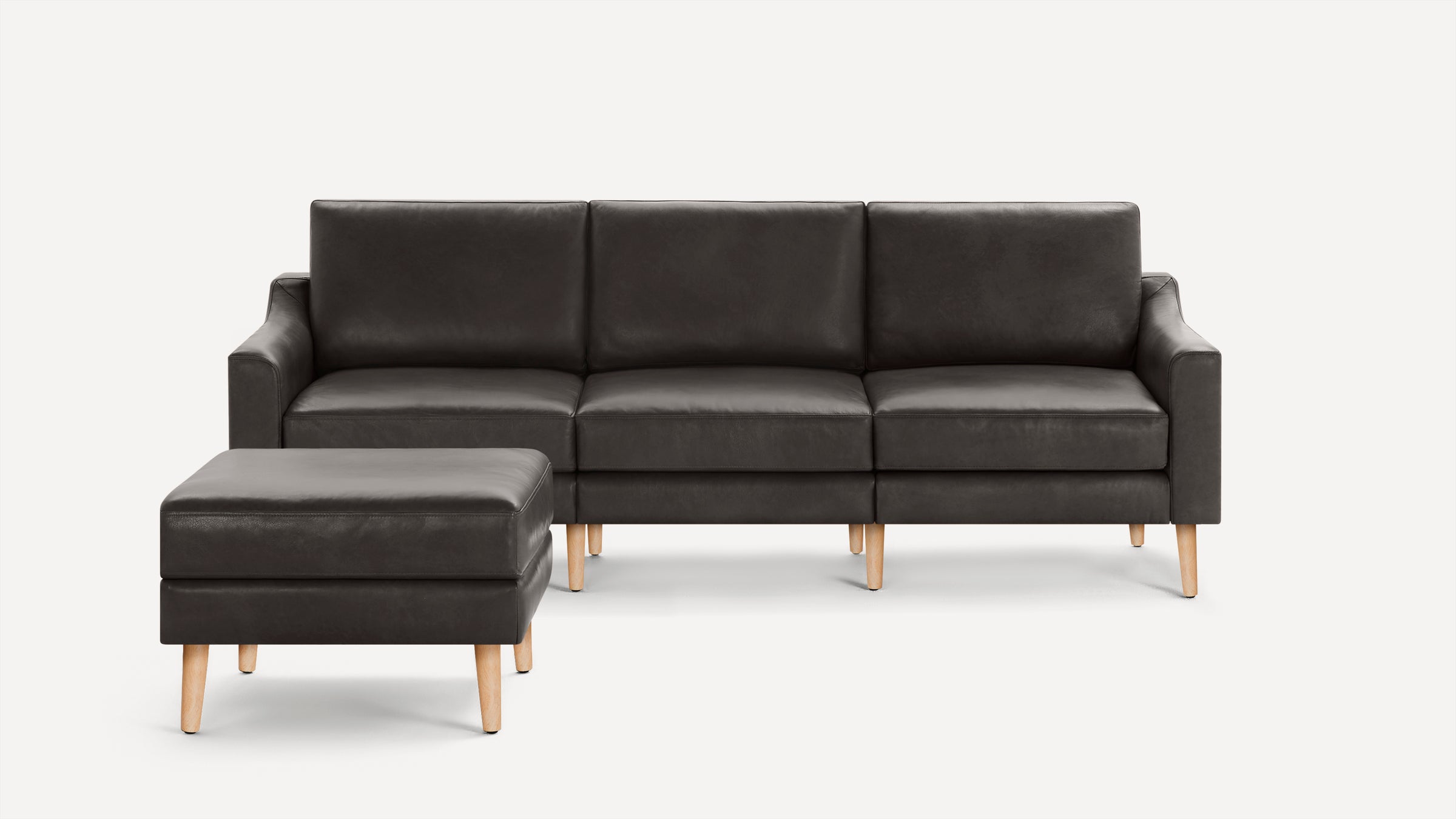 Dark gray three-seater leather sofa with matching ottoman, featuring wooden legs and a modern, minimalist design.