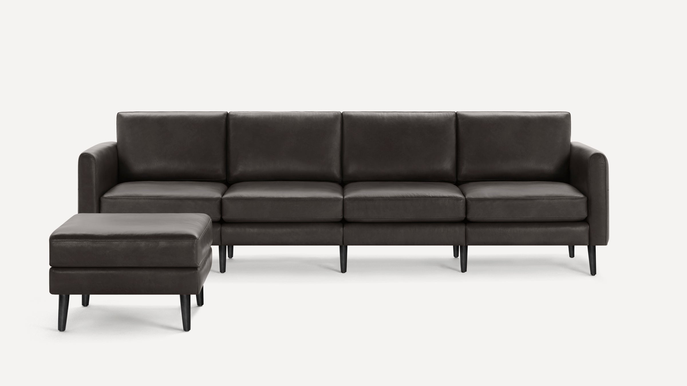 Dark gray leather sectional sofa with four seat cushions and matching ottoman, featuring sleek black legs and modern design.