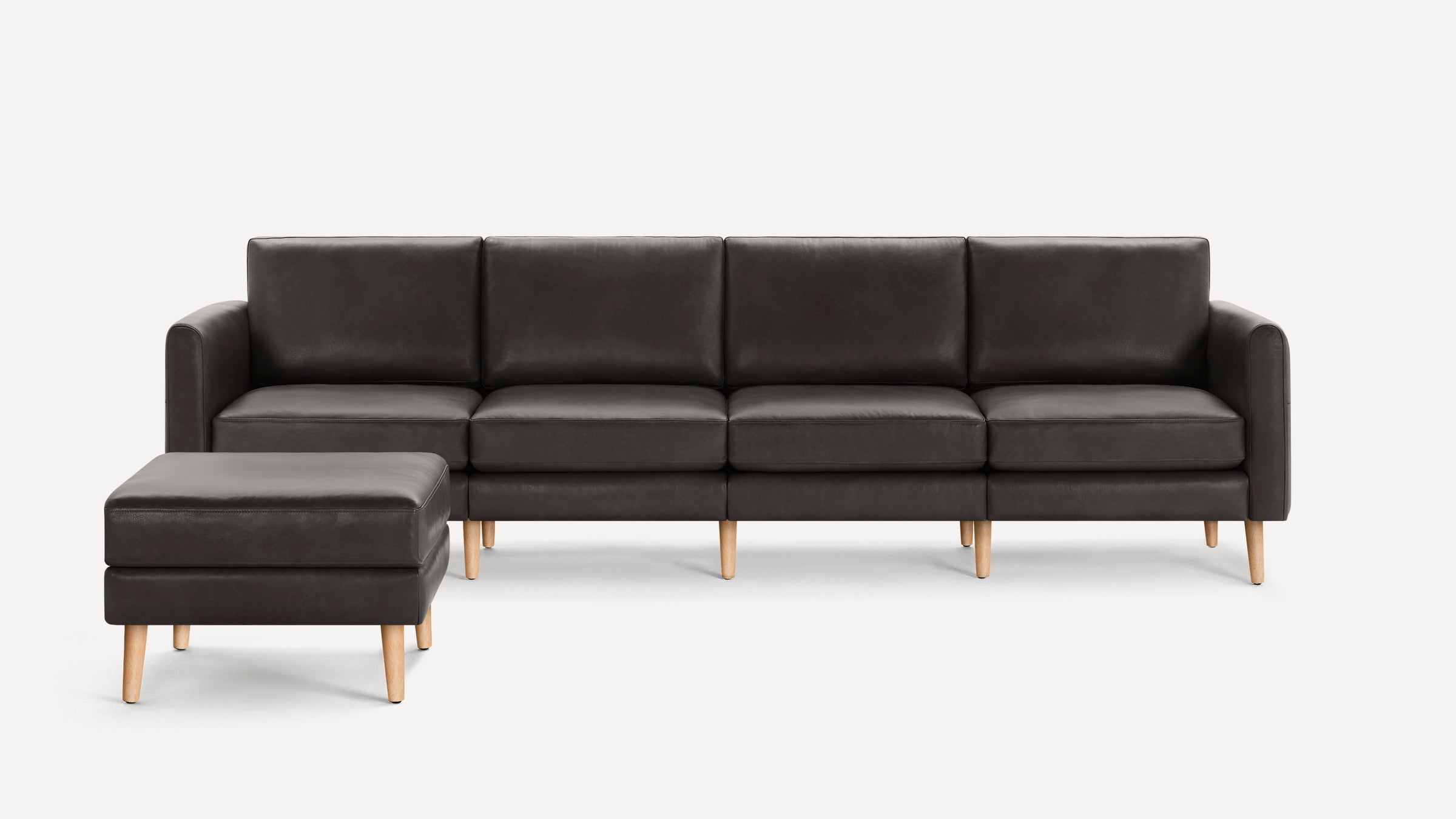 Modern dark gray leather sectional sofa with clean lines, wooden legs, and a matching ottoman, set on white background.