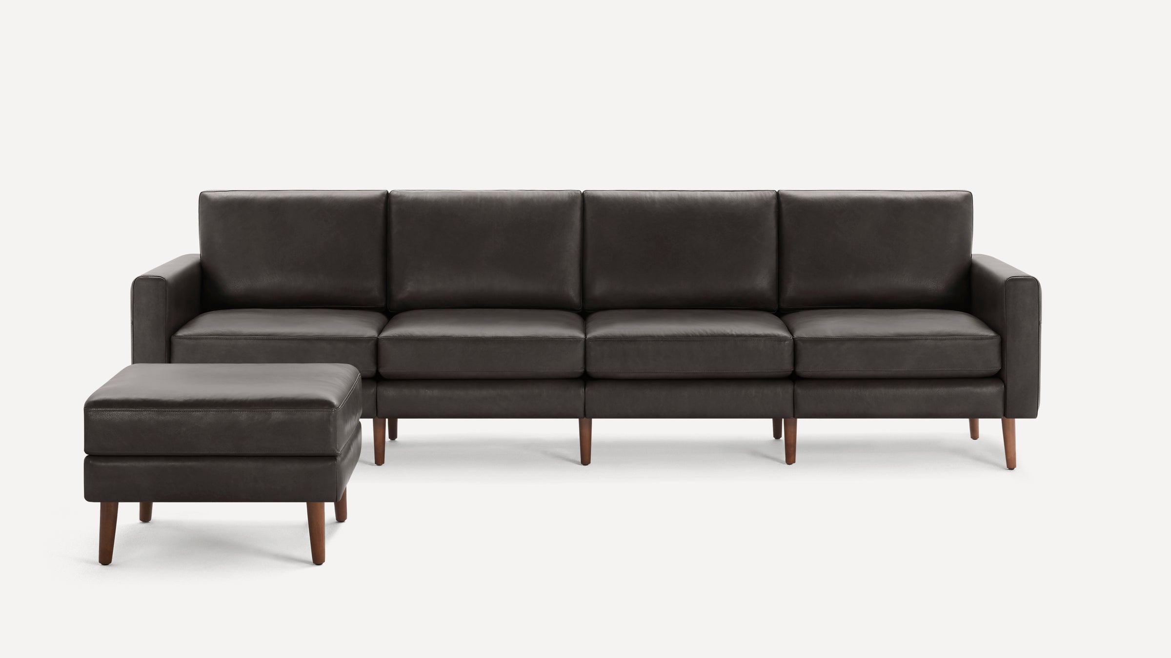 Dark gray leather sectional sofa with clean lines, four seat cushions, matching ottoman, and wooden tapered legs on a white background.