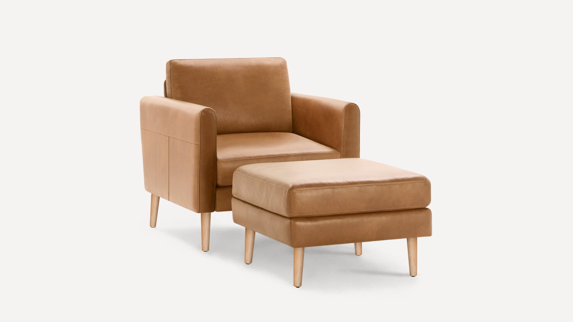 Modern tan leather armchair with matching cushioned ottoman, both featuring light wooden legs against white background.
