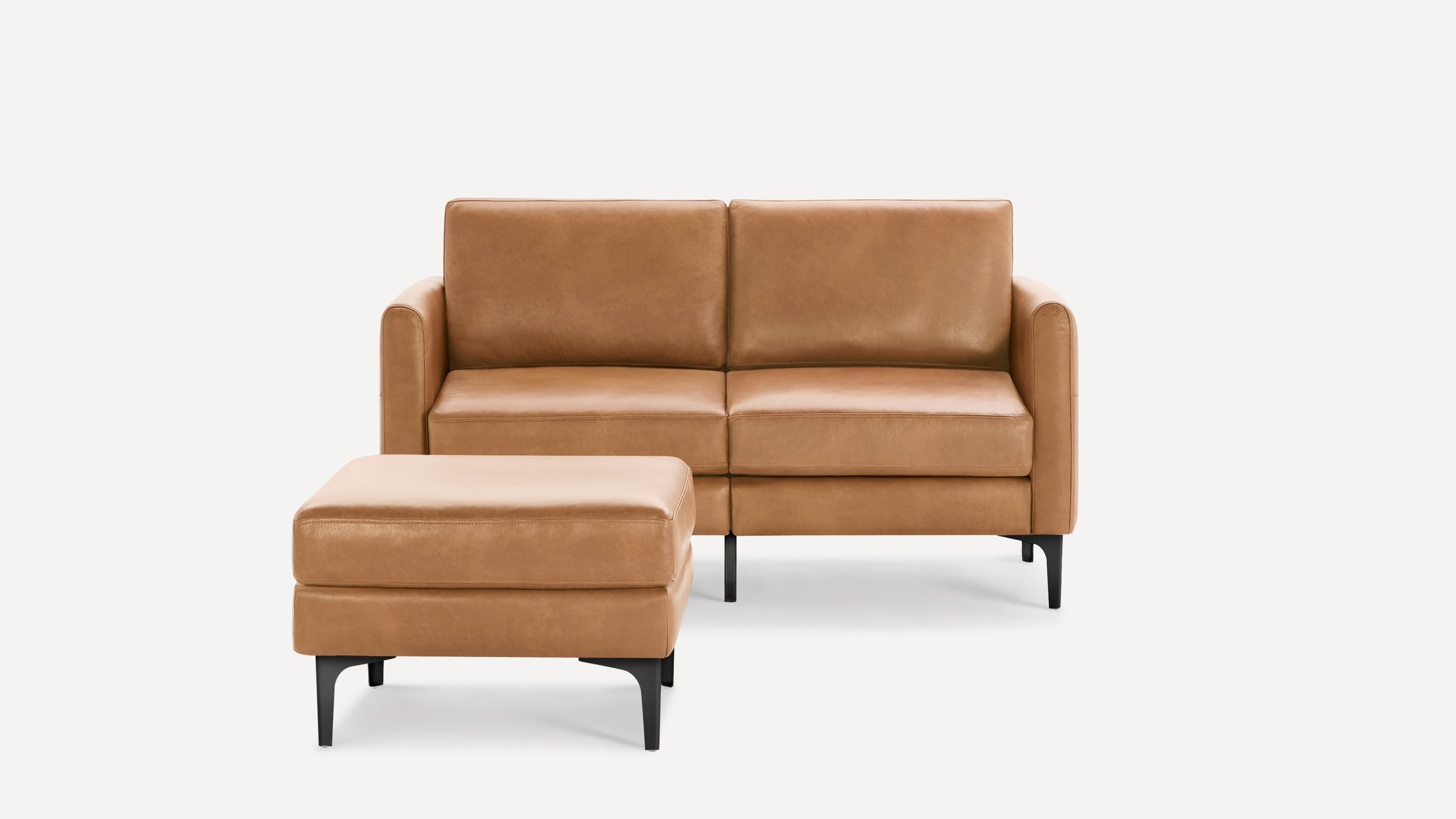 Modern tan leather loveseat with matching ottoman, featuring clean lines and black metal legs on a white background.