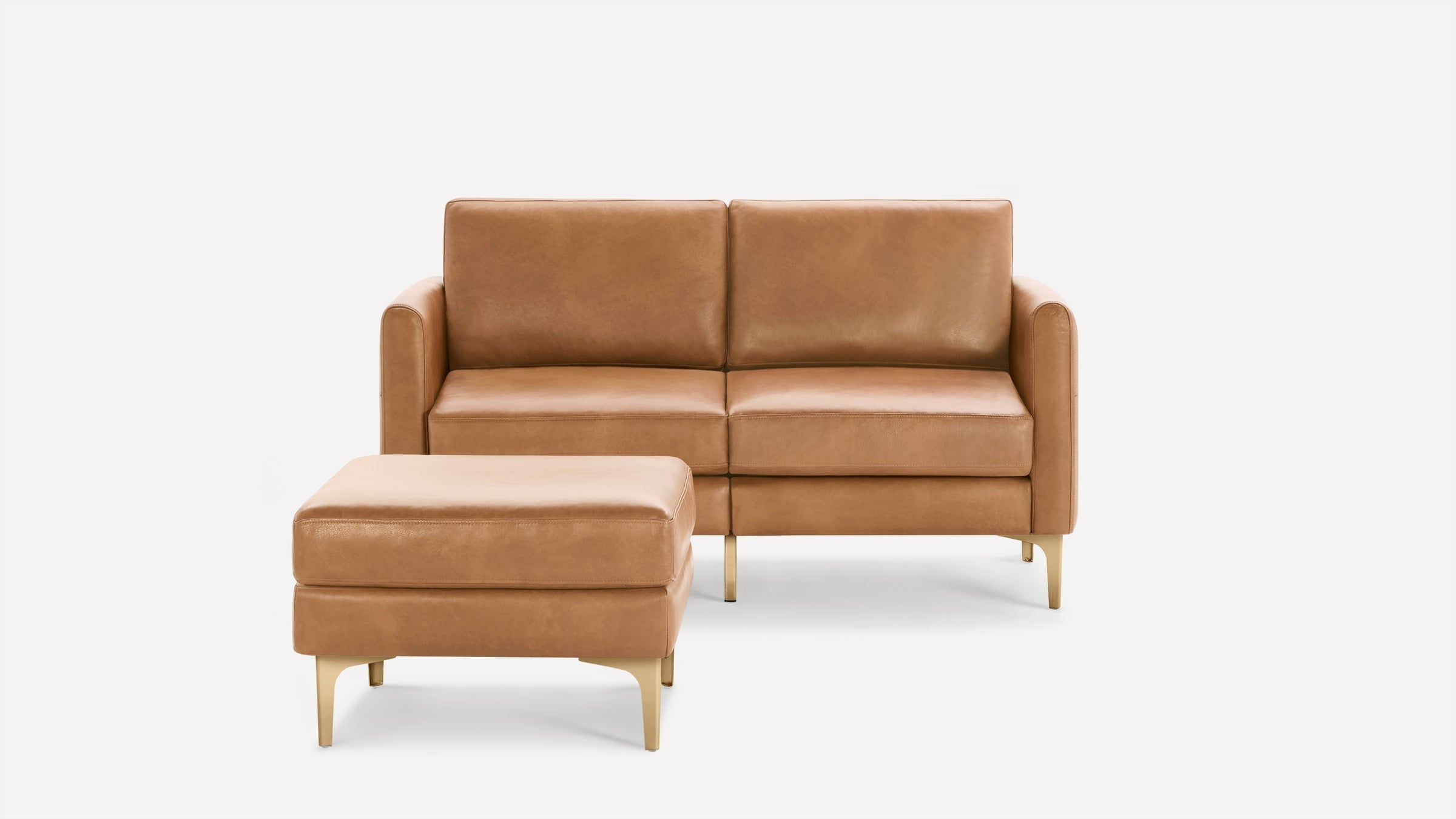 Tan leather loveseat sofa with matching ottoman, featuring sleek modern design and gold-toned legs on white background.