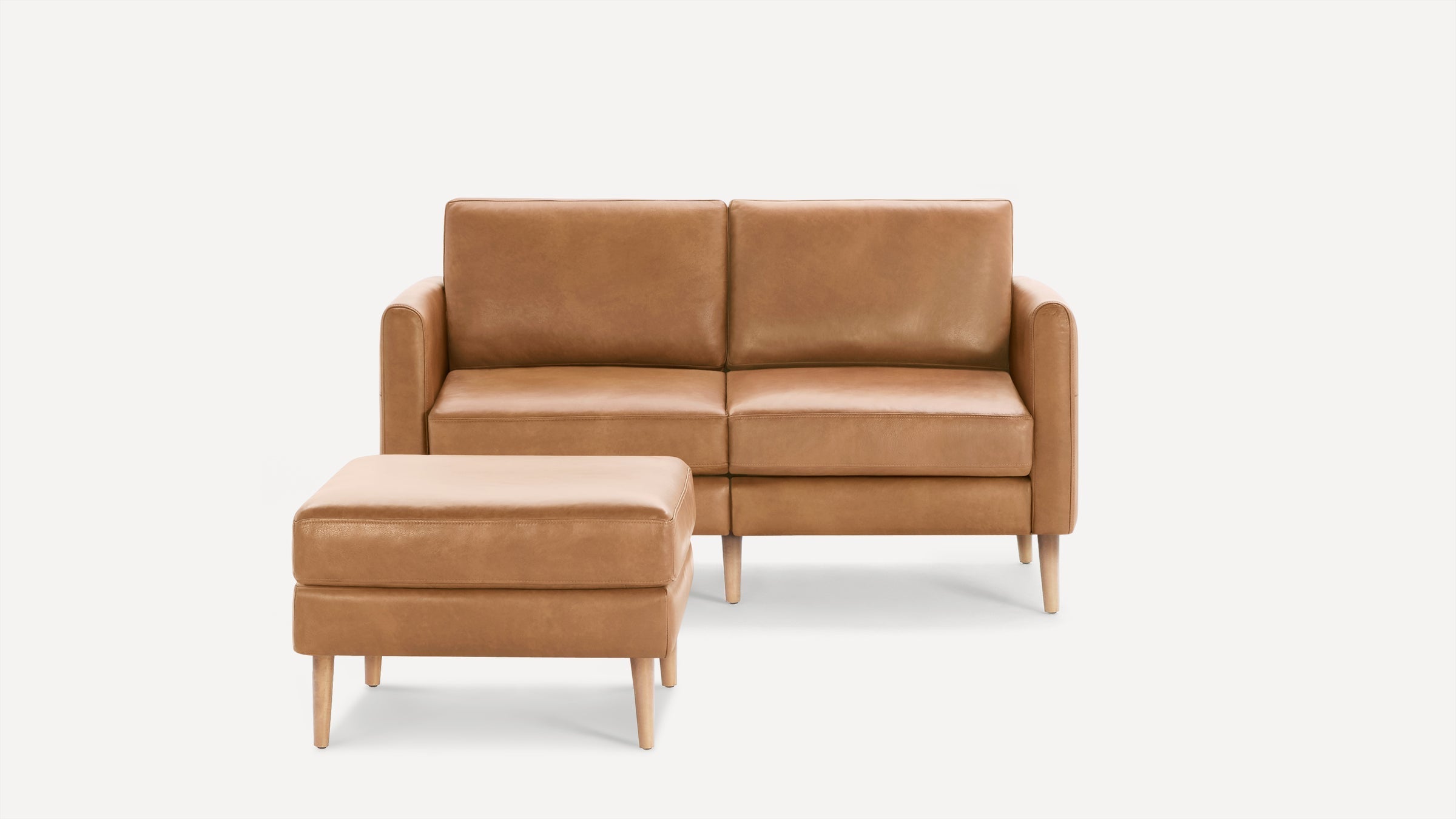 Modern tan leather loveseat with square cushions, straight armrests, and matching ottoman on light wooden legs.