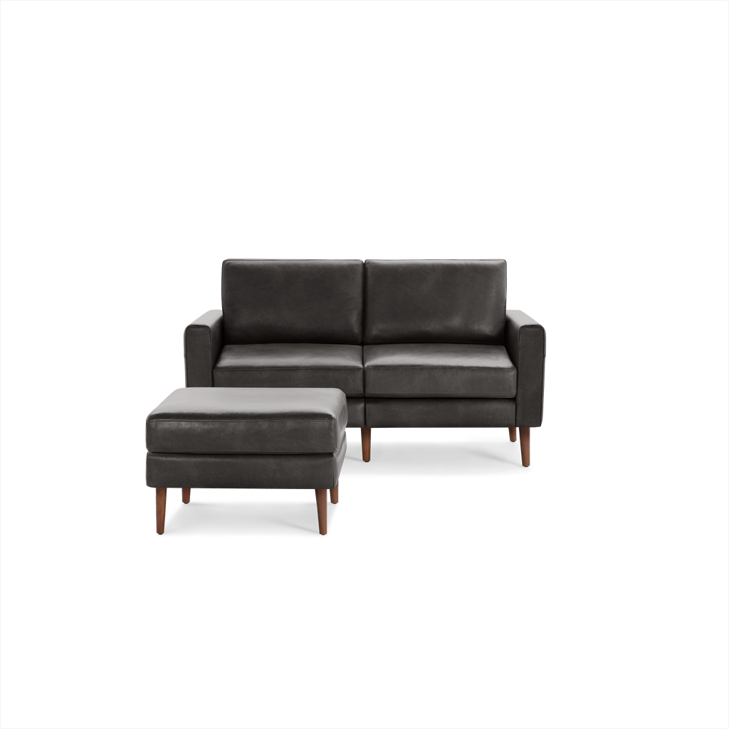 Dark gray leather two-seater sofa with matching ottoman, both featuring wooden legs and a modern, minimalist design.